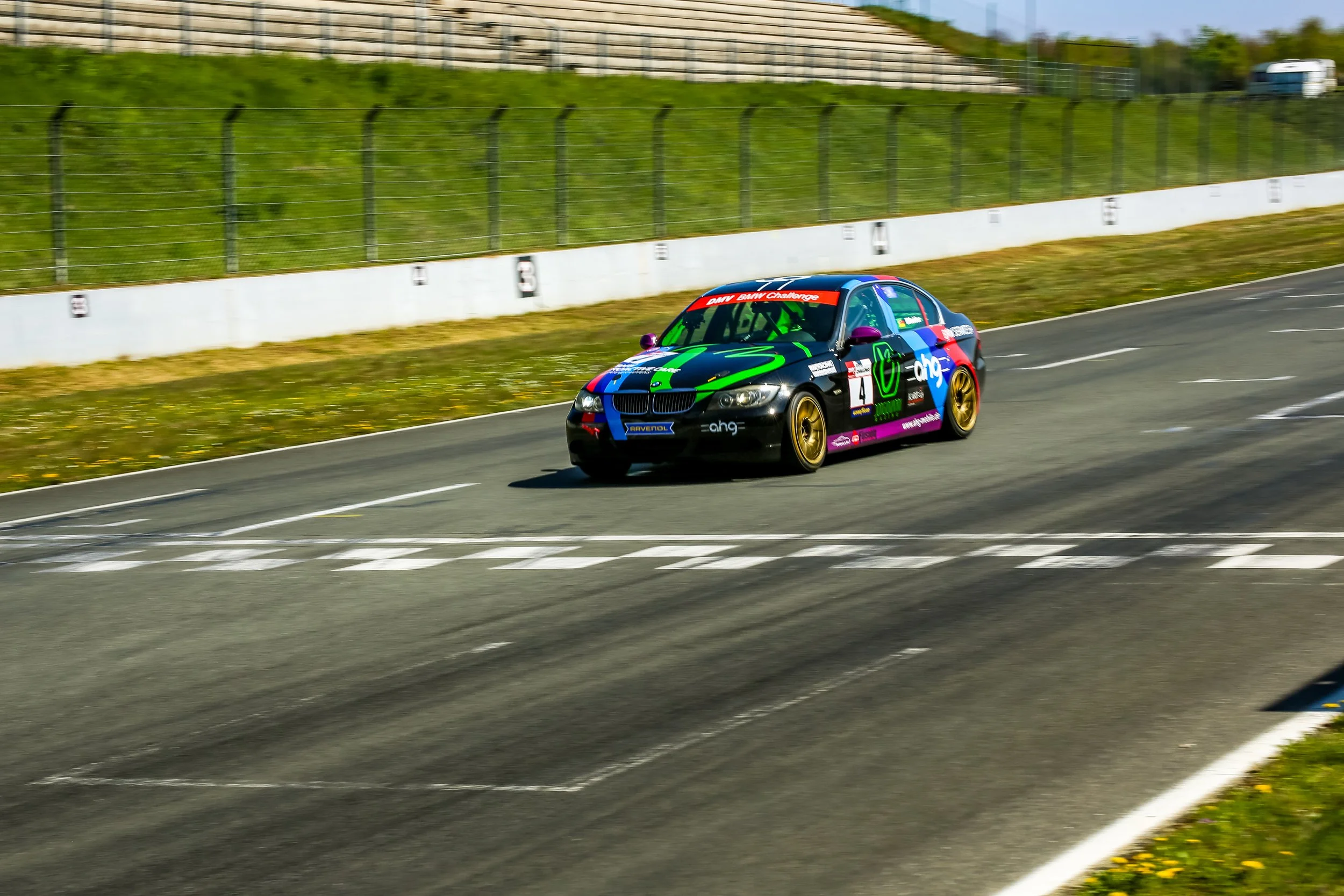 Colorful race car on a track with grass and a fence in the background during daytime.