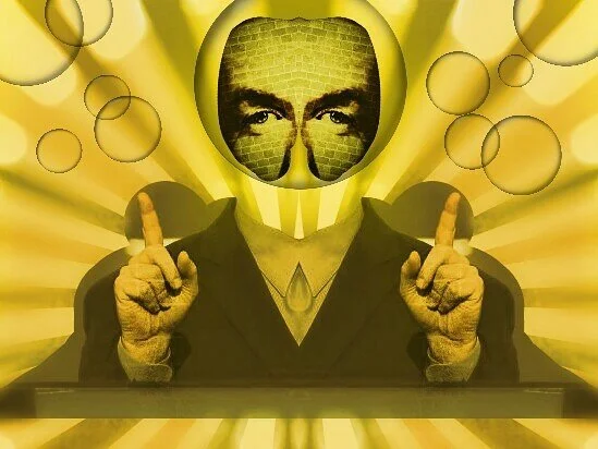 A person wearing a suit with a face replaced by a large circular image of a man's eyes and eyebrows, with a green brick wall in the background. The person has both hands raised with index fingers pointing upward.