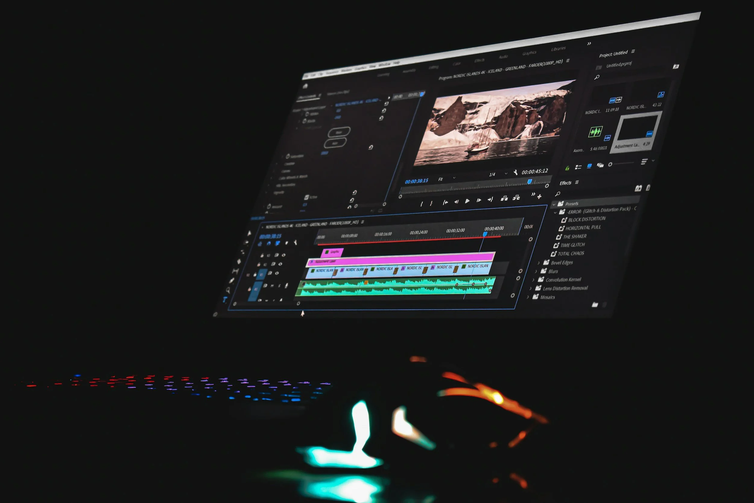 A computer monitor displaying a video editing software with a nature scene of icebergs, rocky cliffs, and a boat in water, with colorful audio tracks and editing tools visible.