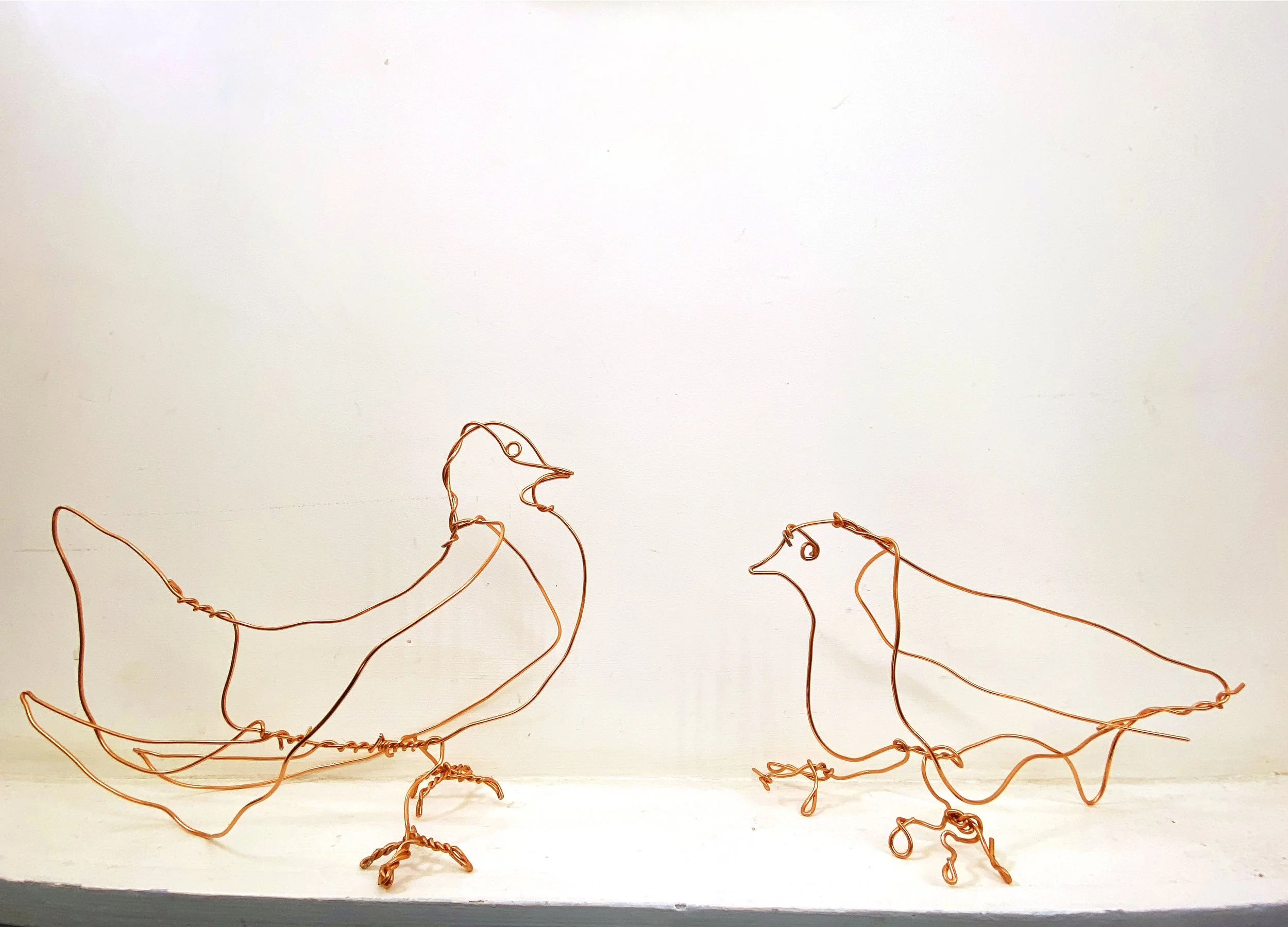 Decorative copper wire art depicting abstract animal figures on a white background.