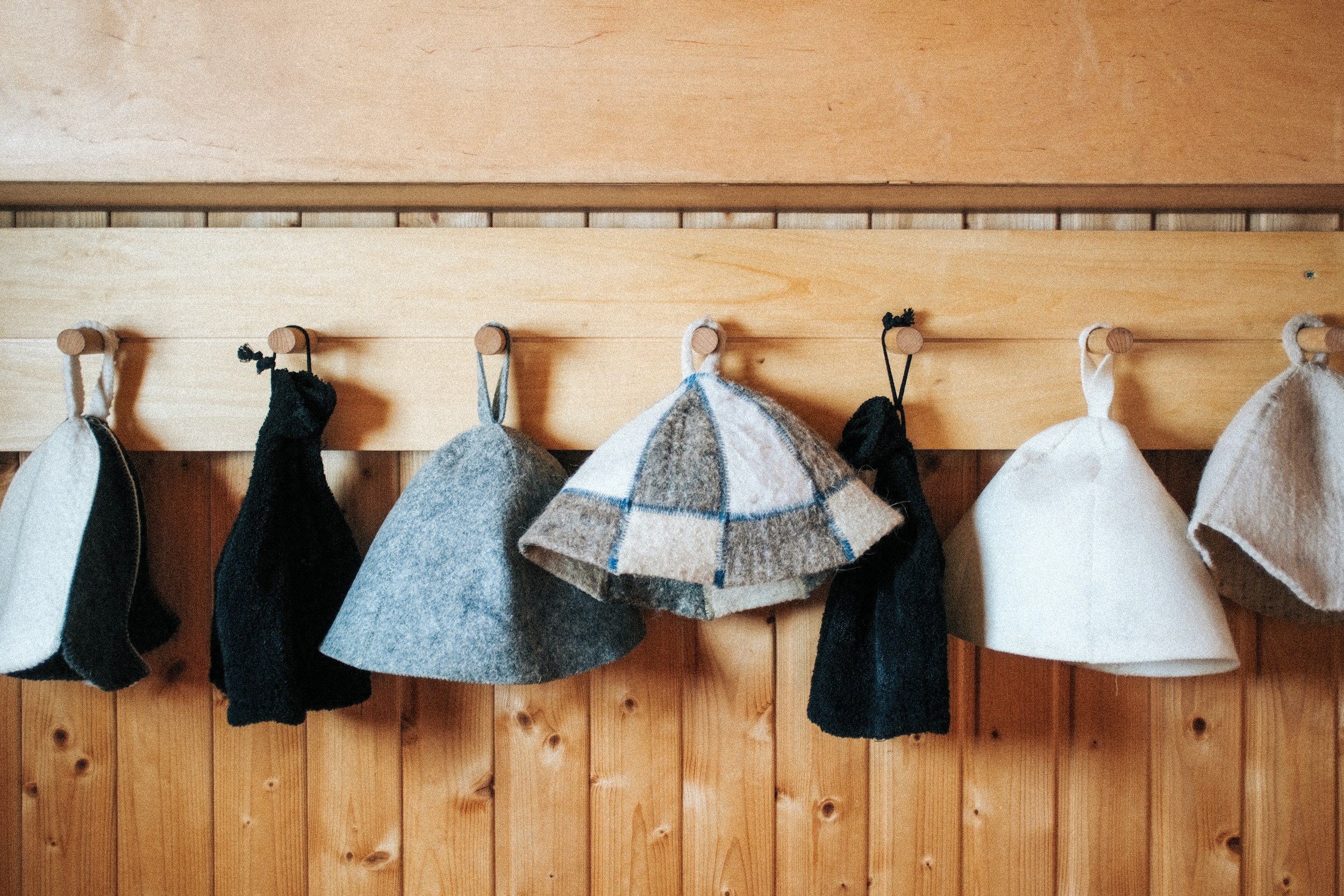 Wooden wall with hooks holding various black, gray, and white socks and a cap.