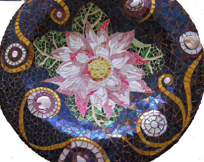 Colorful mosaic artwork featuring a central white and pink flower with green leaves, surrounded by swirling patterns in blue, gold, and white.