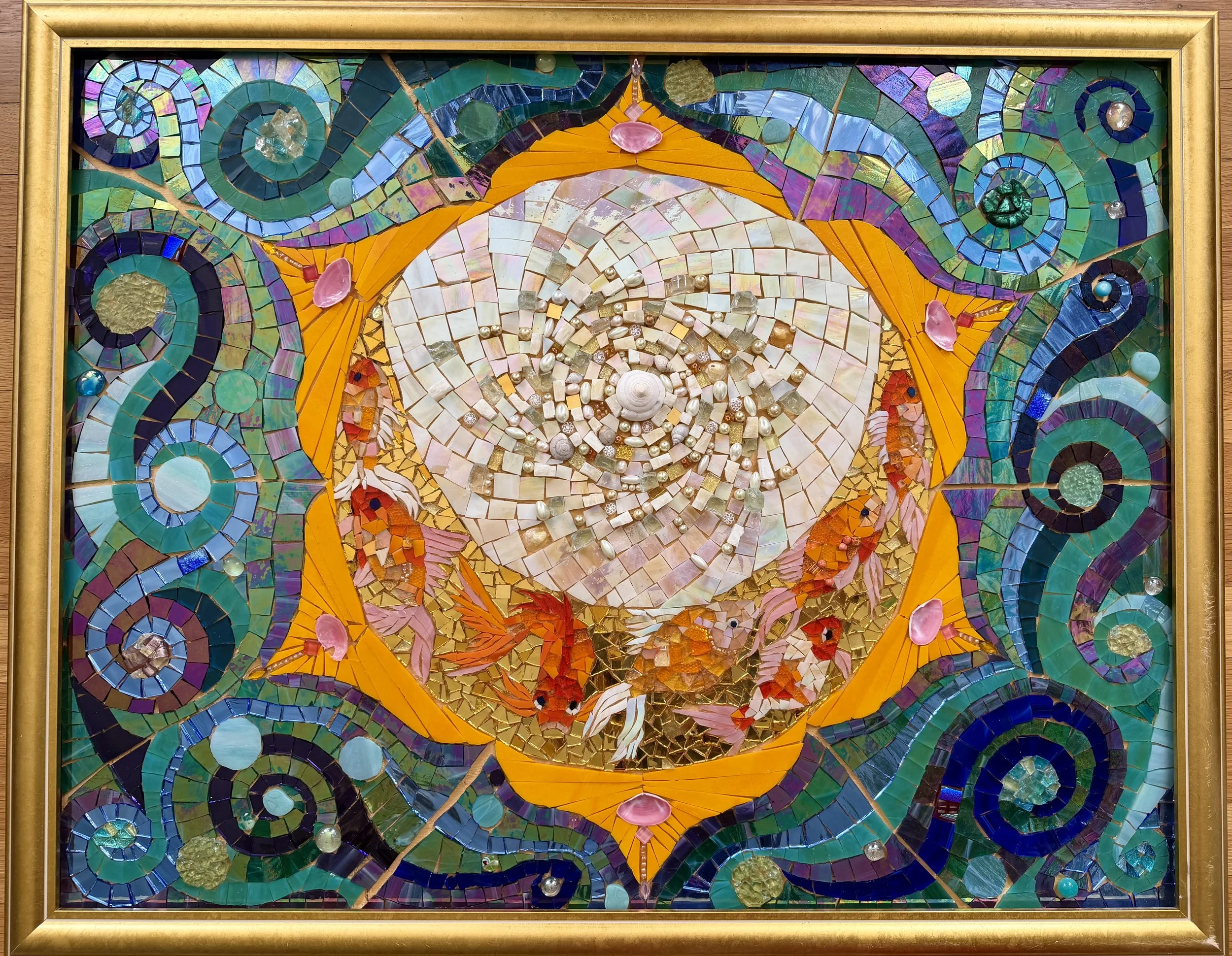 Colorful mosaic artwork featuring a central image of a stylized owl with large eyes, surrounded by swirling patterns, shells, and various glass and ceramic pieces in vibrant colors.