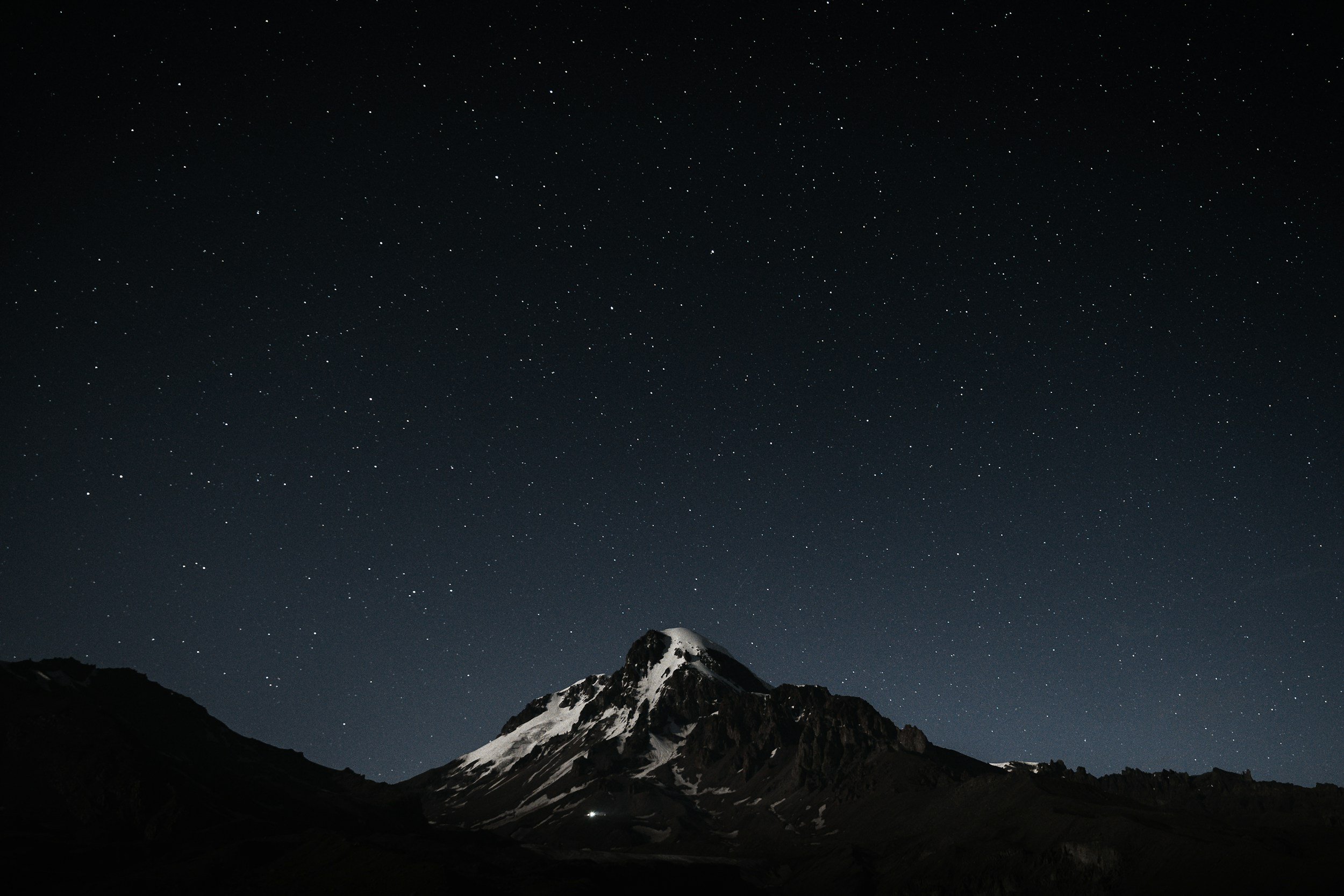 Nighttime view of a mountain with snow-capped peaks under a star-filled sky.