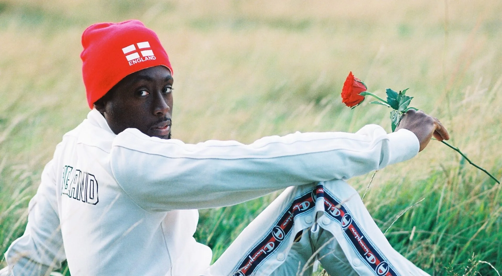 Nadeem Din-Gabisi in white tracksuit top with a red England hat, holding a rose