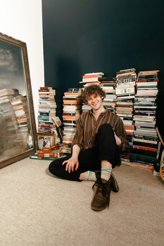 Bill Ryder Jones sat smiling in front of stacks of books