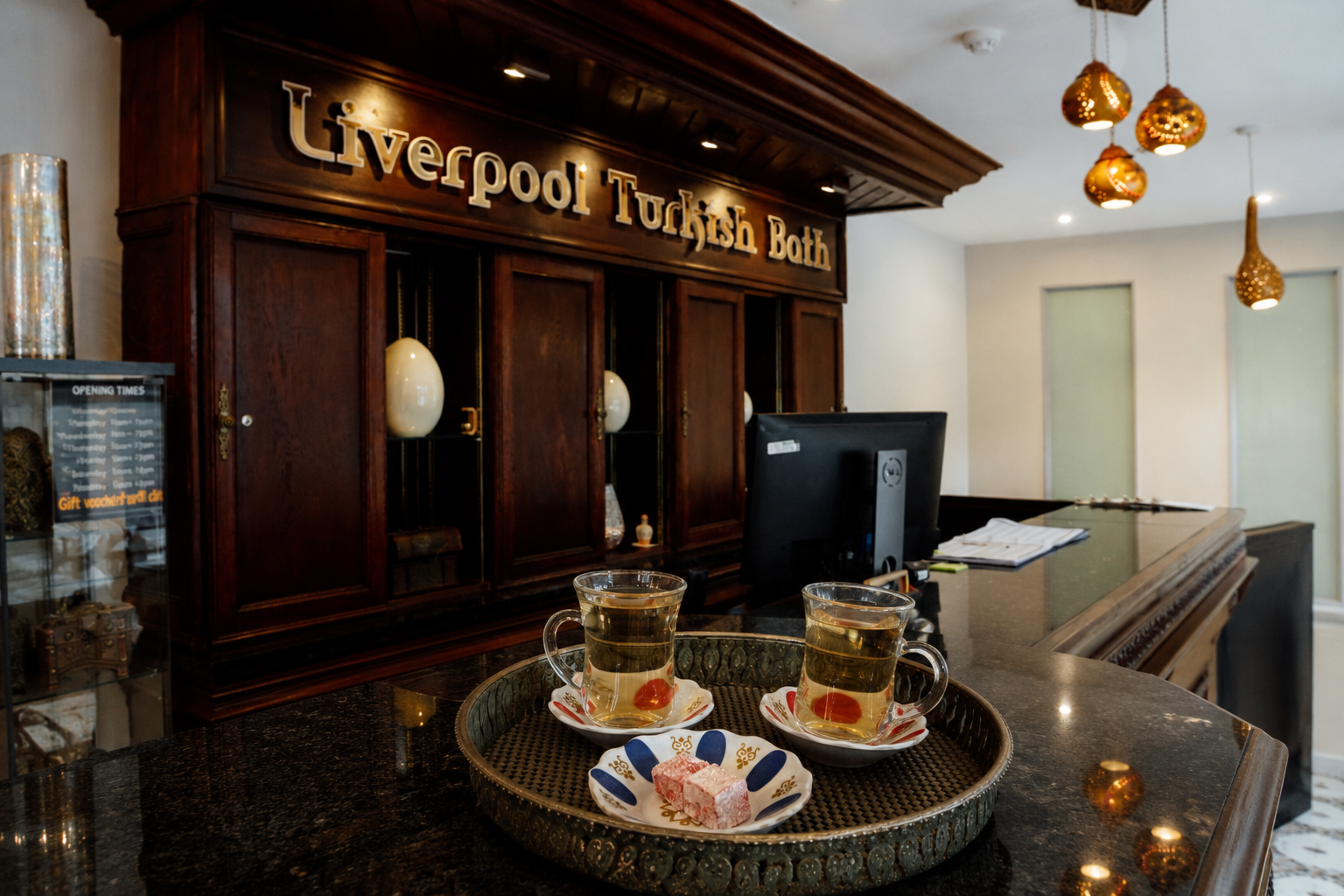 Tray with two cups of Turkish tea and Turkish delight on a dark marble counter at a Turkish restaurant. In the background, a wooden sign reads "Liverpool Turkish Bath."