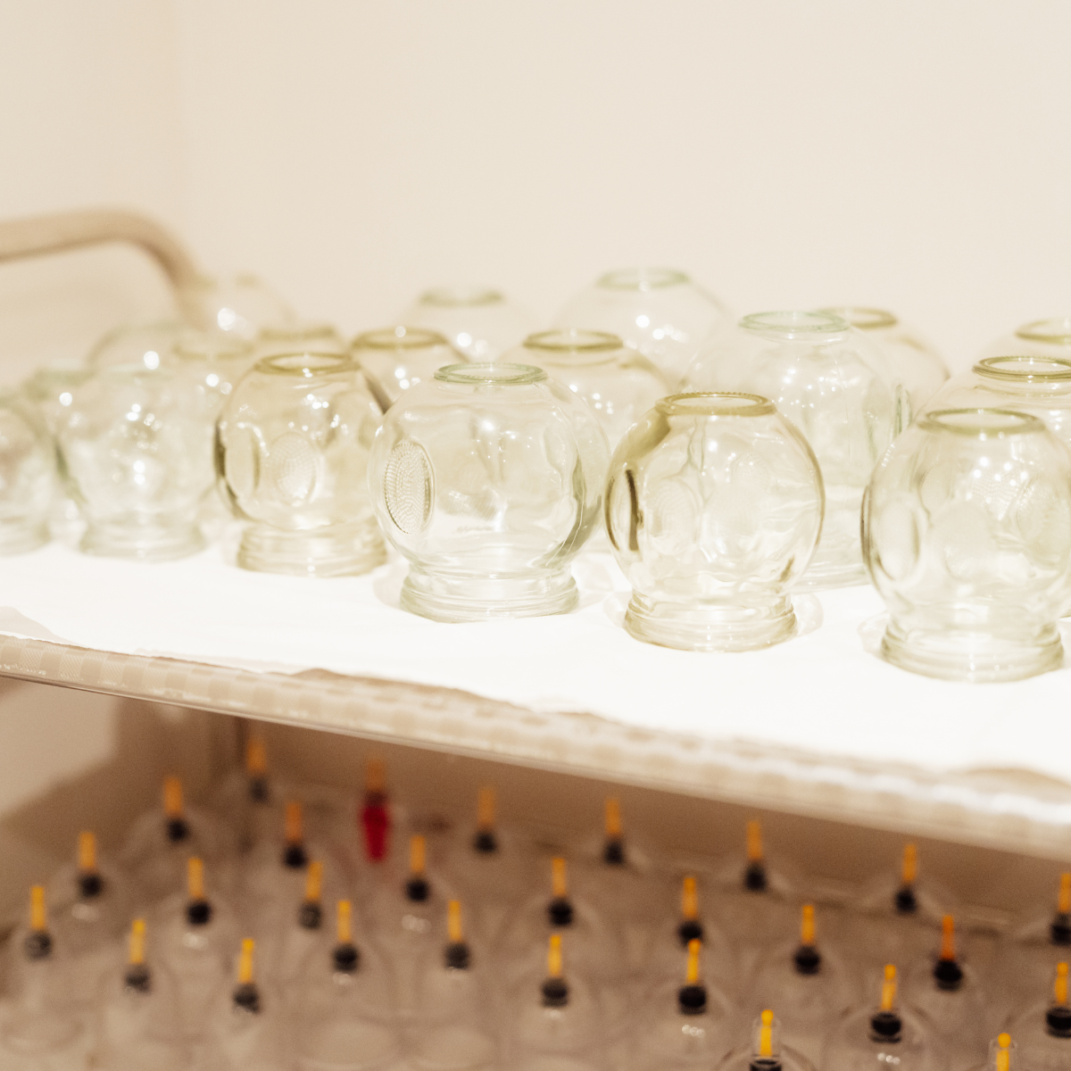 Multiple empty glass jars lined up on a white surface with a blurred background of small bottles with droppers.