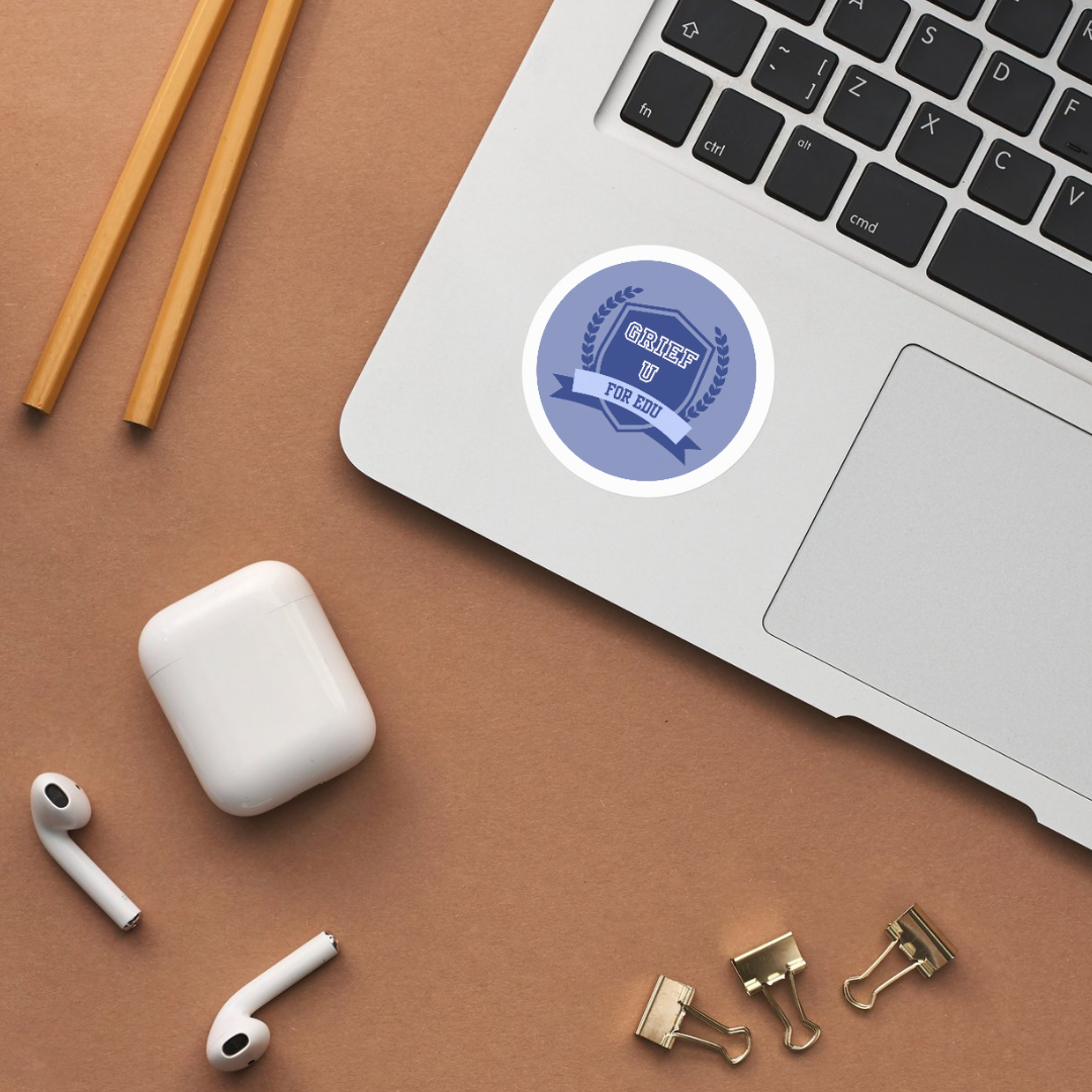 A laptop with a blue badge sticker on the corner, a pair of yellow chopsticks, wireless earbuds with a charging case, and gold binder clips on a brown surface.