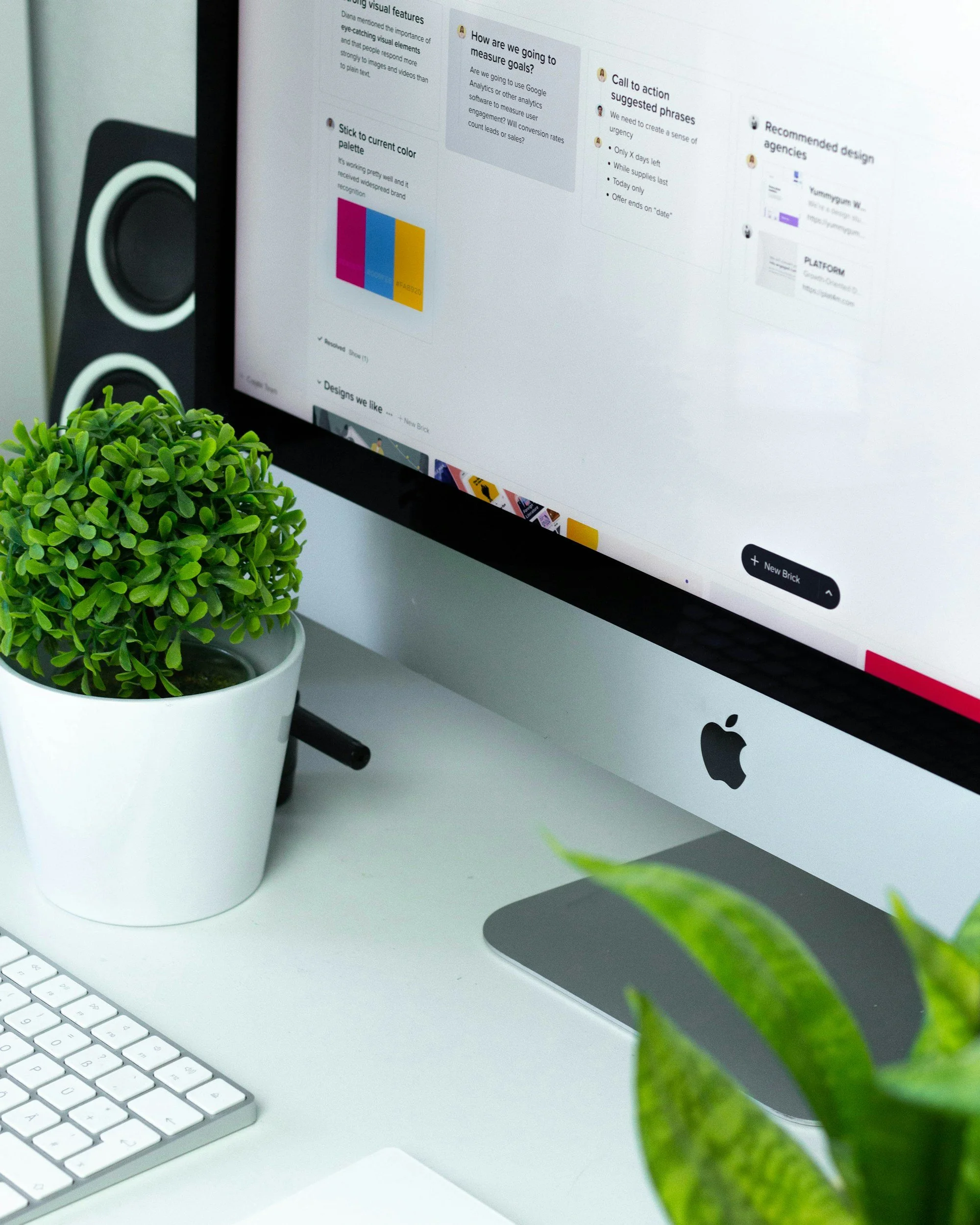 Close-up of a computer screen displaying a digital note with text, a pie chart, automations, workflows, and a section labeled 'How are we going to measure goals?' next to a green potted plant on a white desk with a white keyboard.