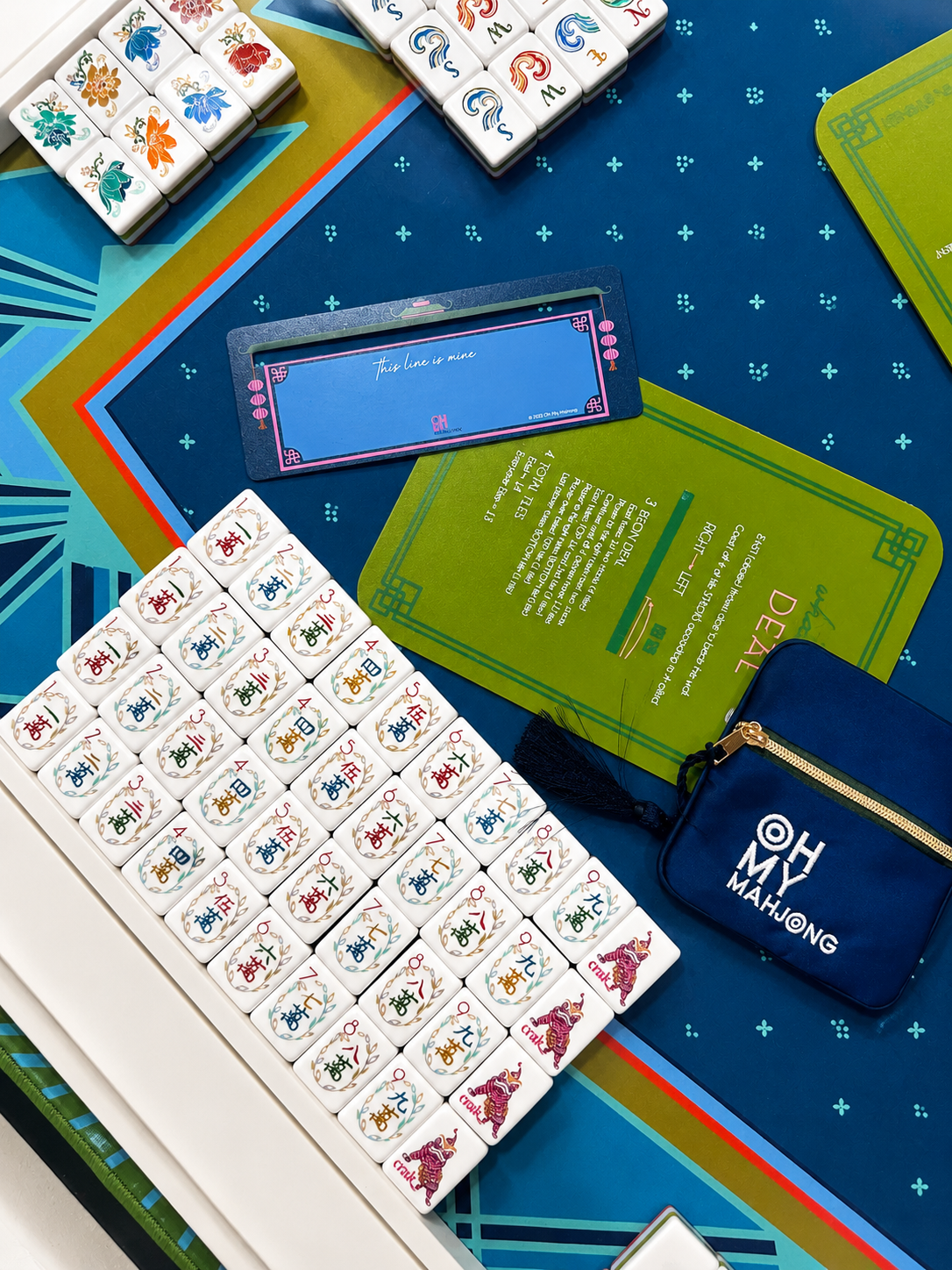 American mahjong game setup on a colorful table with tiles,scorecards, and a blue pouch labeled 'OH MY MAHJONG'.