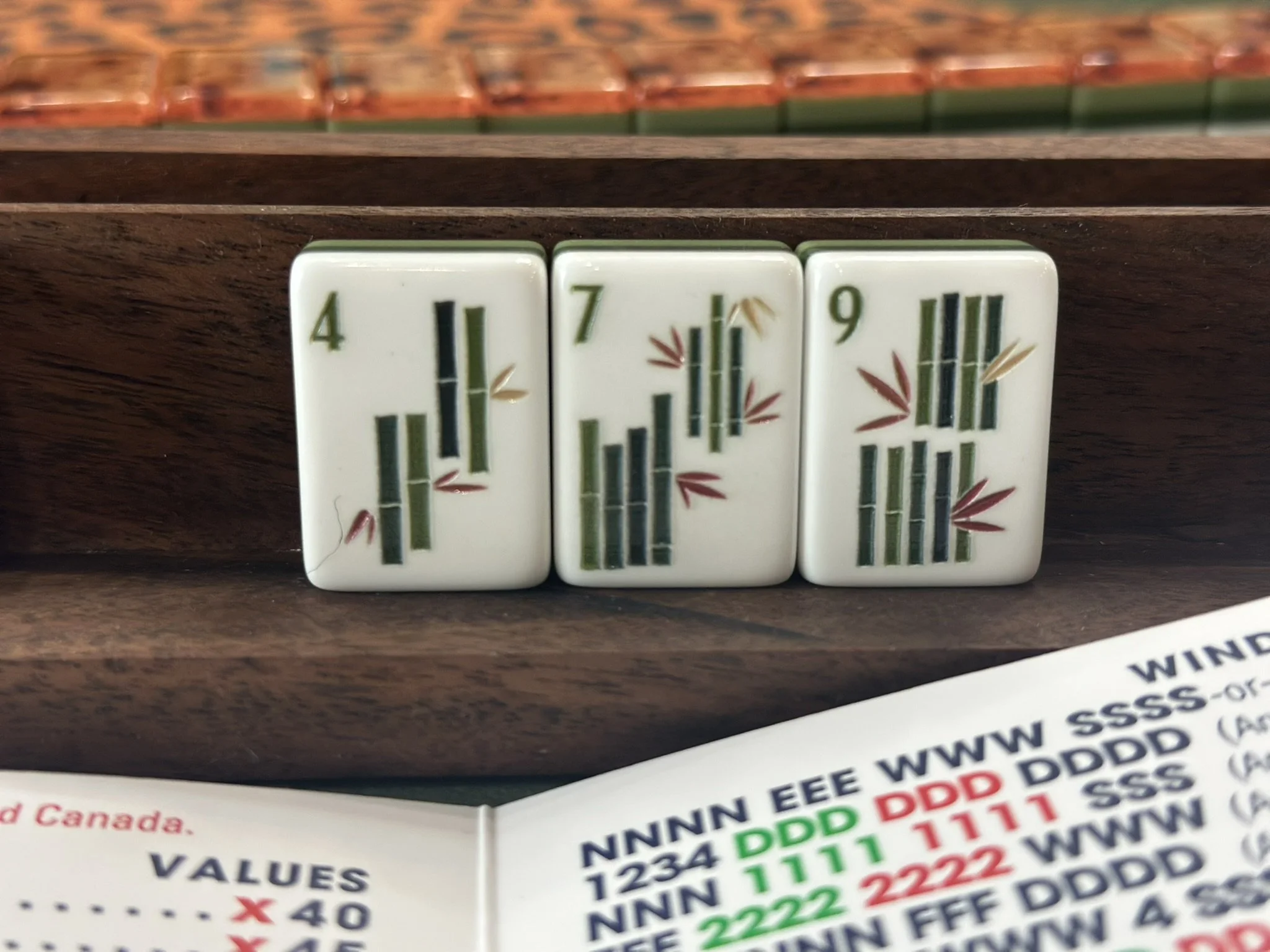 Close-up of American Mahjong tiles on a wooden surface with various numbers and symbols.