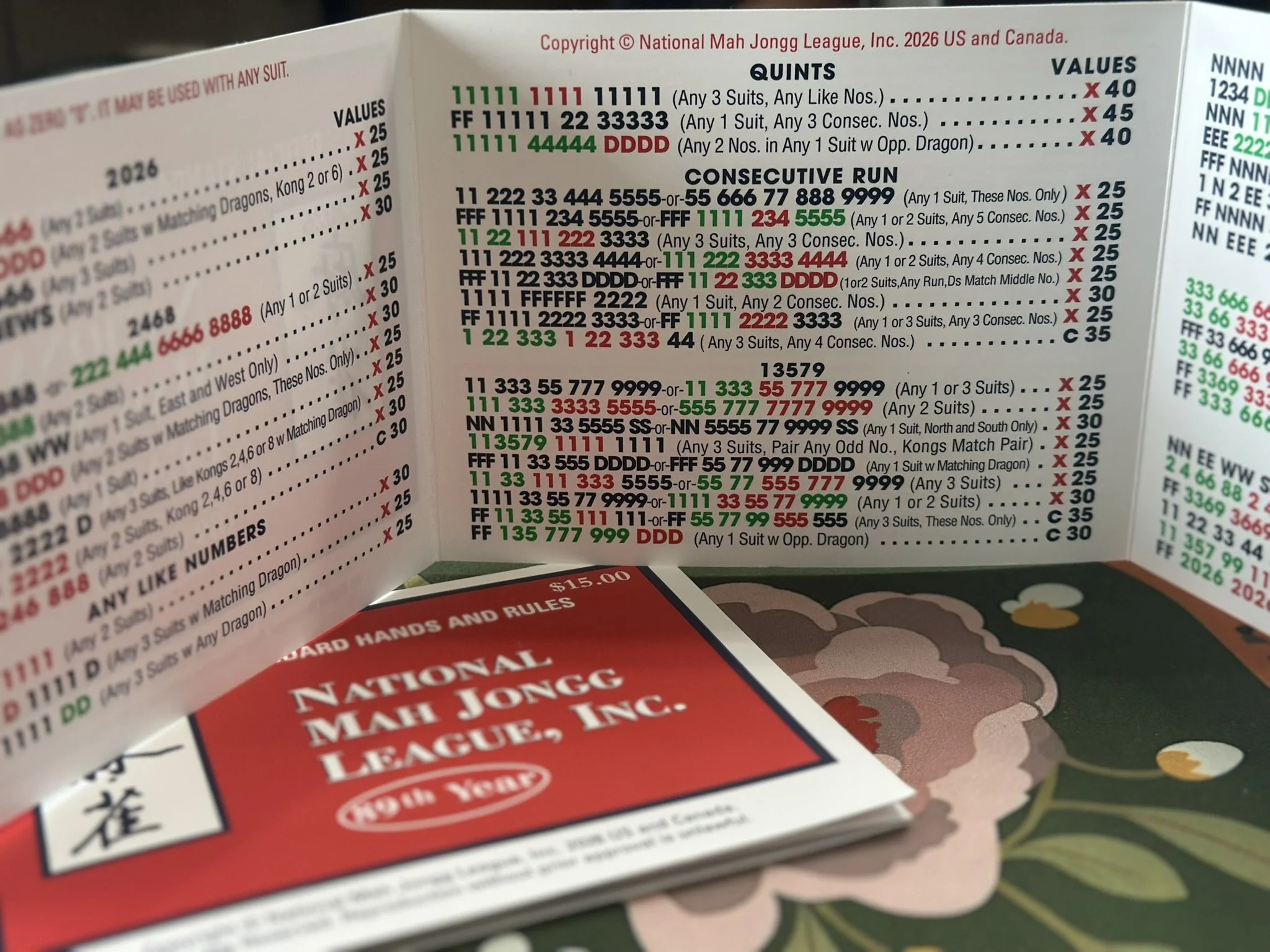 Close-up of a colorful cheat sheet for American Mahjong scoring, showing different hand patterns and their point values, with red, black, green, and blue text.