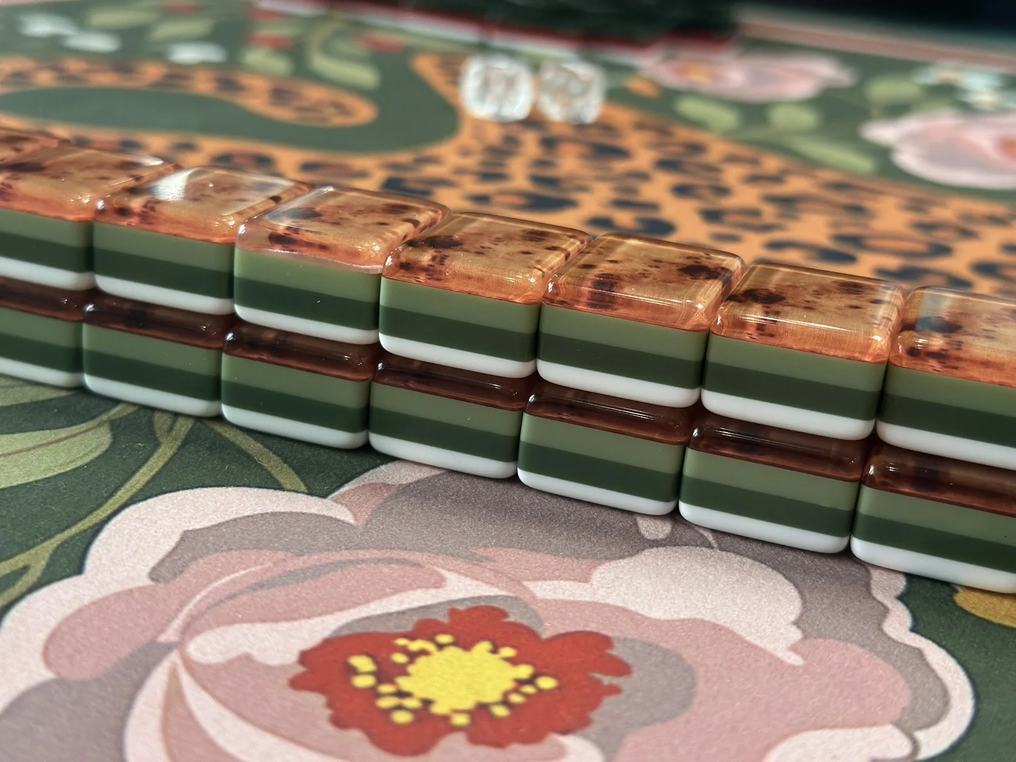 Close-up of stacked American mahjong tiles with floral and solid designs on a patterned surface.