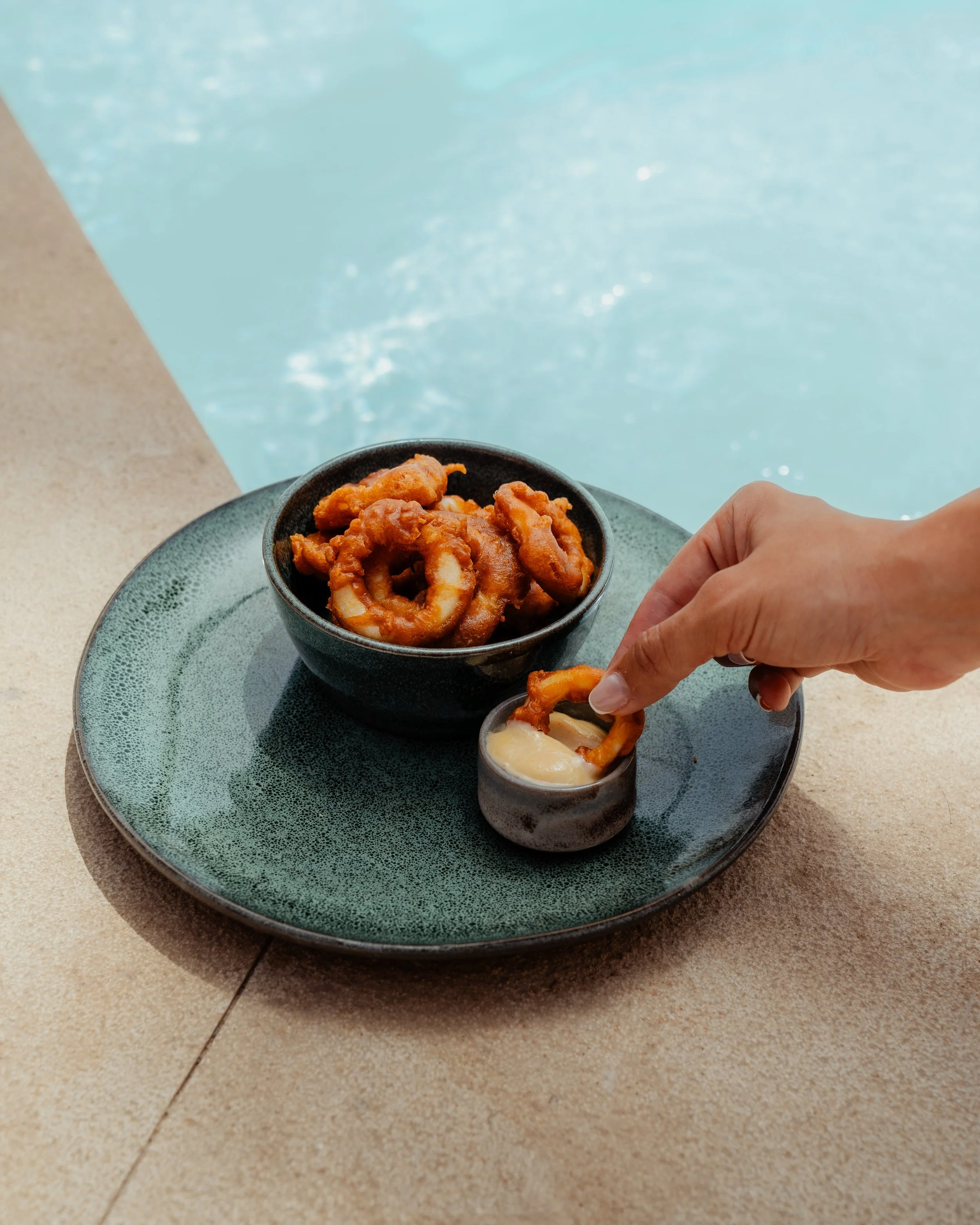 Un bol de calamars frits, accompagnés d'une sauce blanche, sur une assiette sur une table à proximité d'une piscine en plein air.