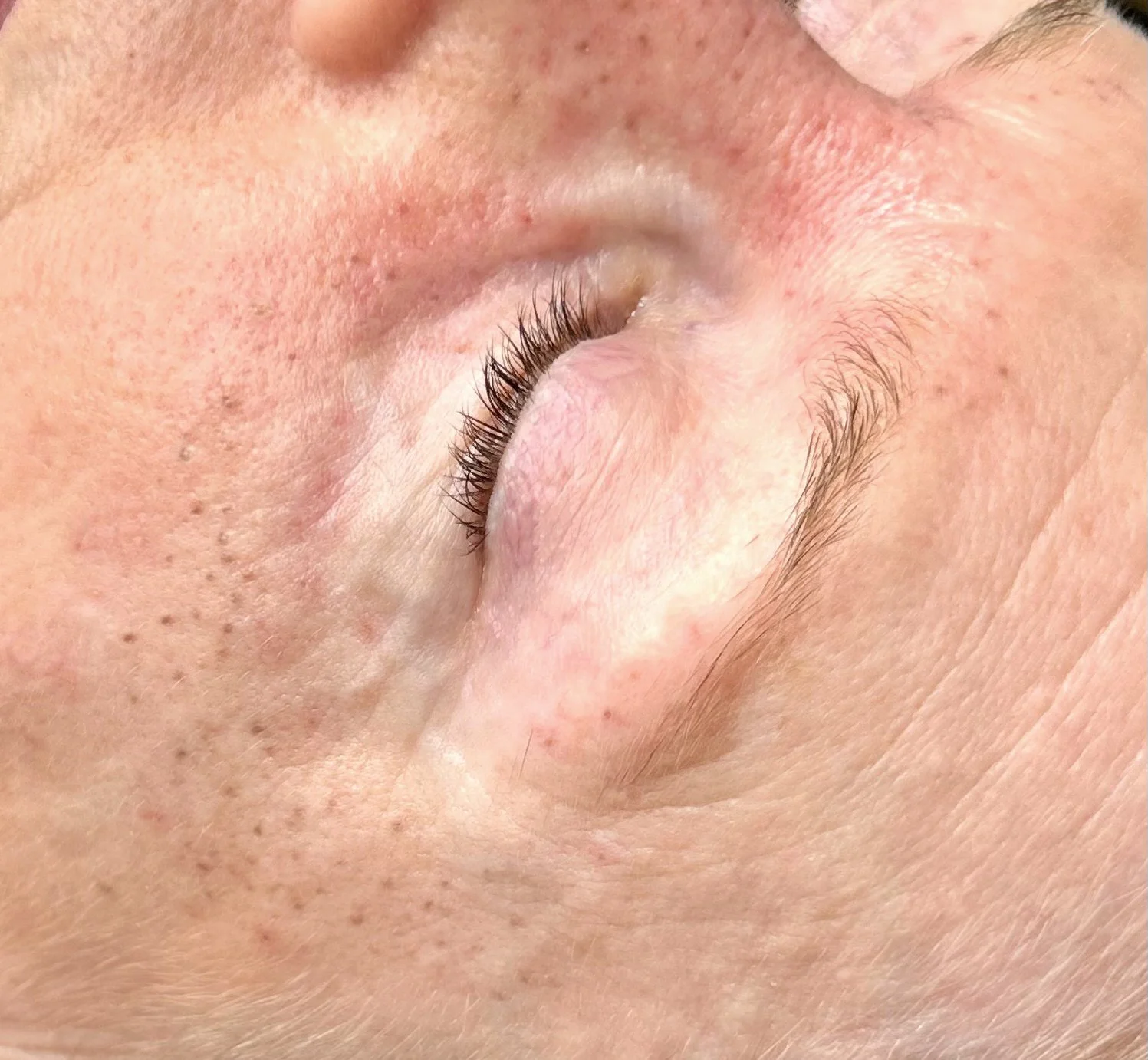 Close-up of a closed human eye with long eyelashes, eyebrow hair, and visible facial skin texture.
