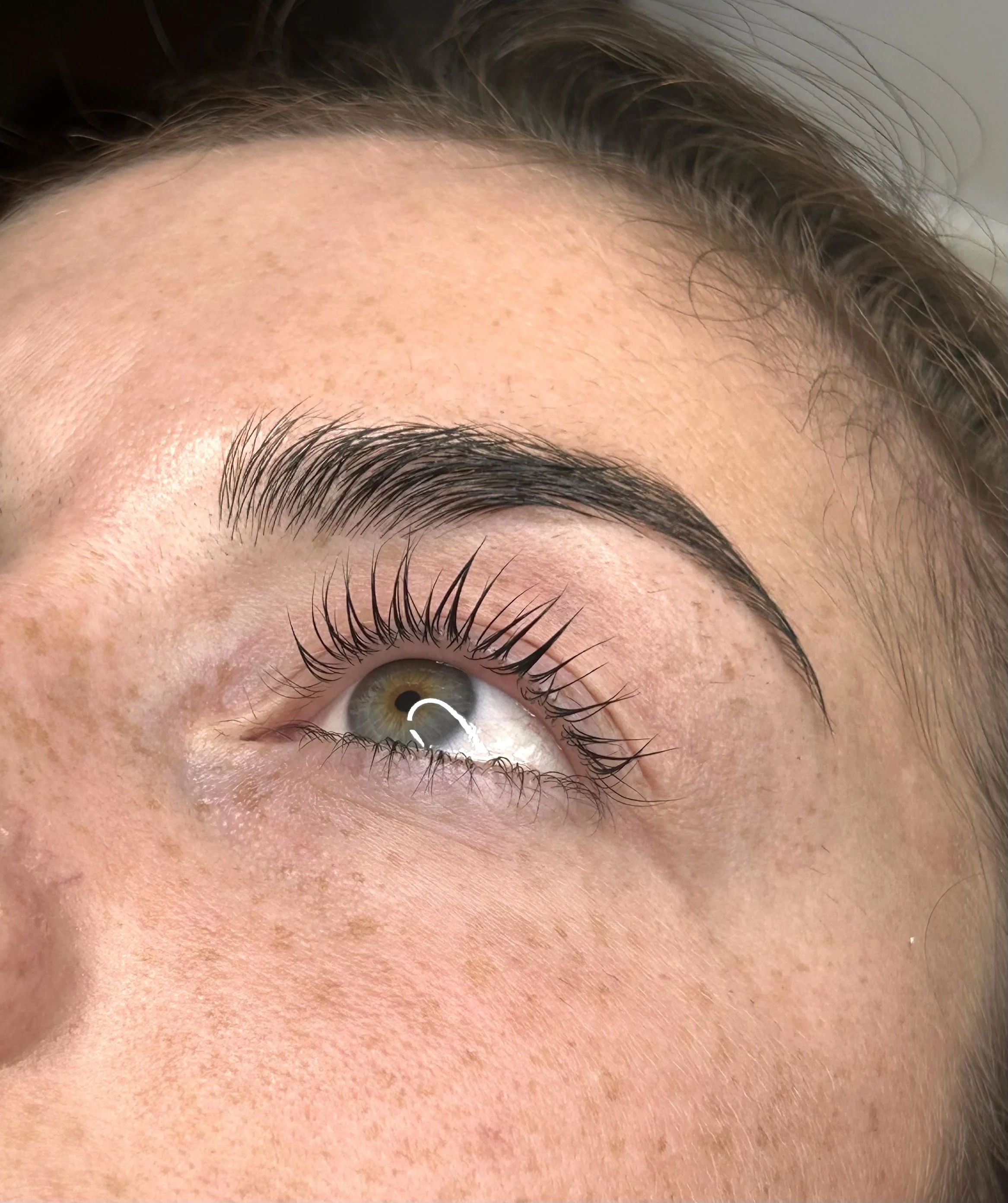 Extreme close-up of a person’s green-hazel eye, eyebrow, eyelashes, and surrounding skin.