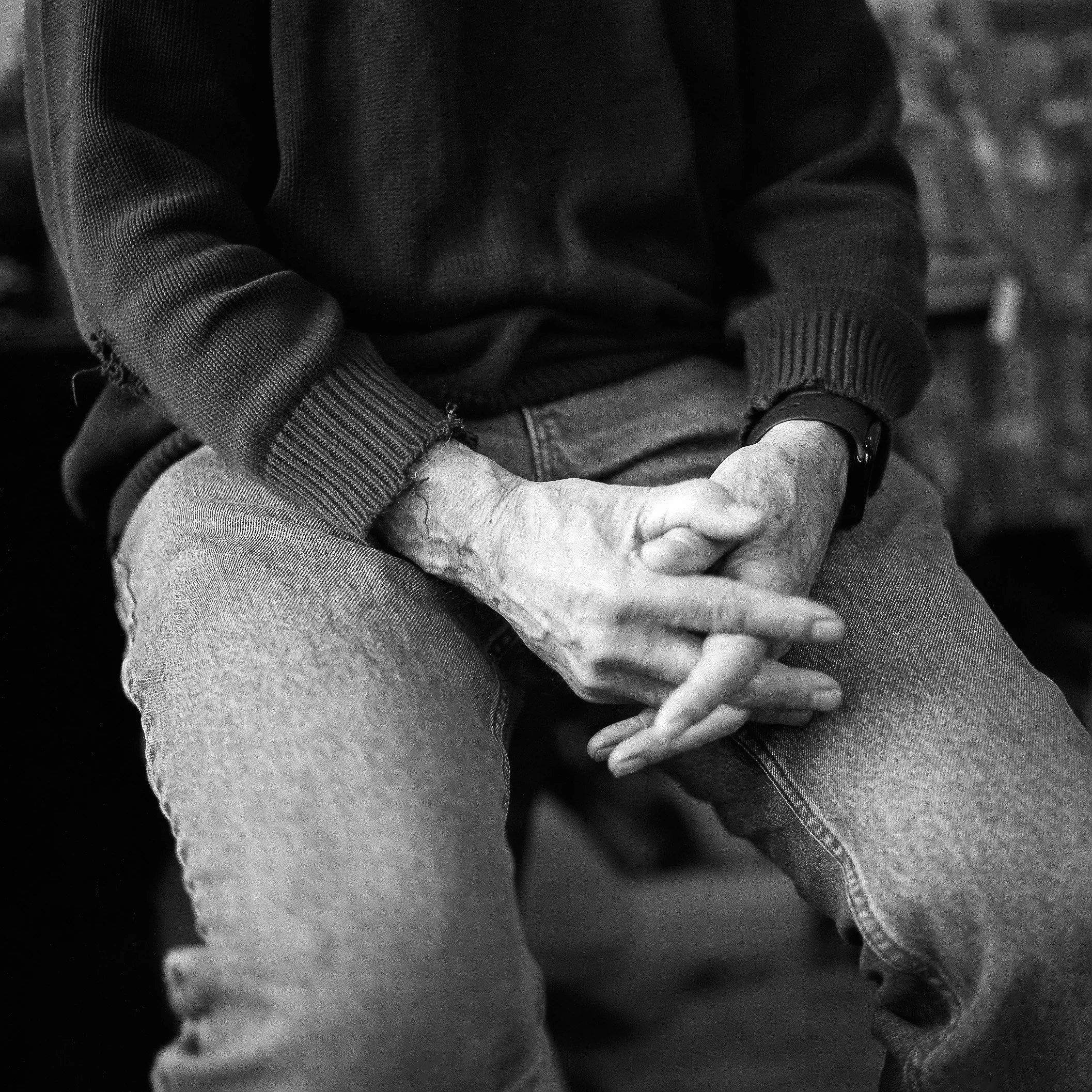 Close-up of two people holding hands, one with light skin and the other with darker skin, wearing casual clothing including a hoodie and denim jeans.