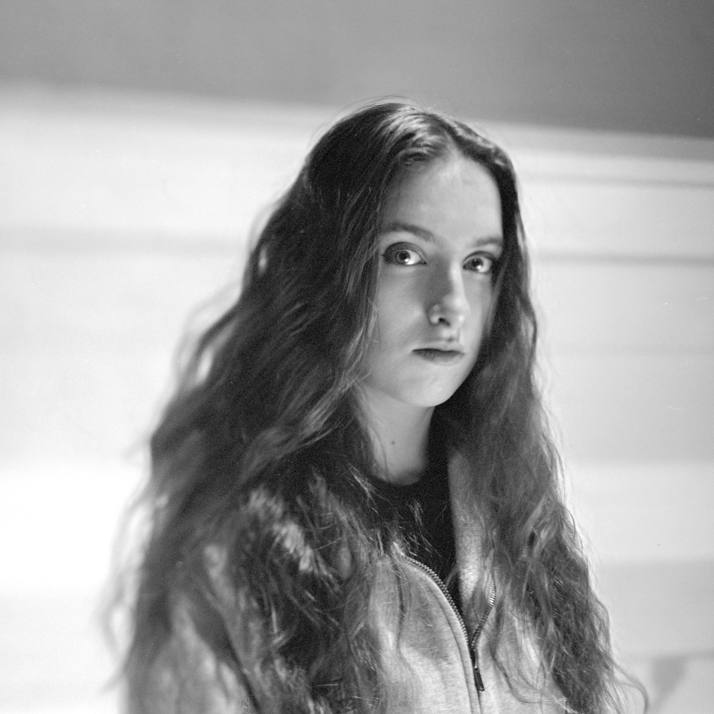 A black and white close-up of a woman with long wavy hair, looking upwards.