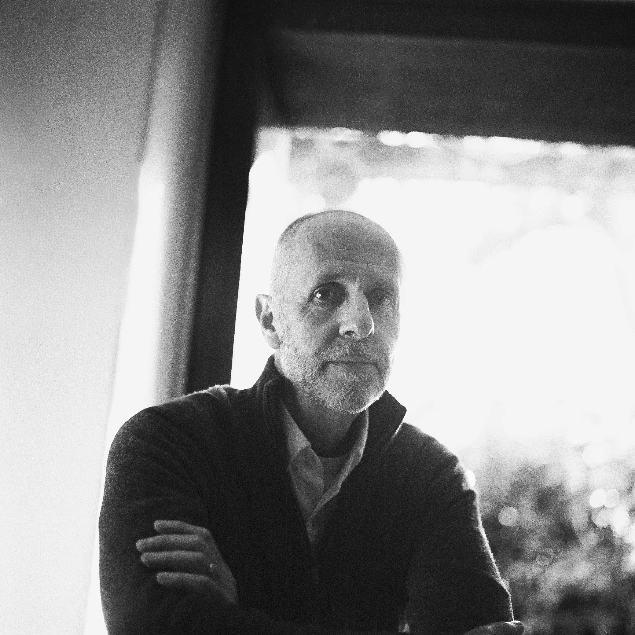 A black and white close-up photo of a man holding a smartphone, with a focus on his face and hand, against a blurred outdoor background.