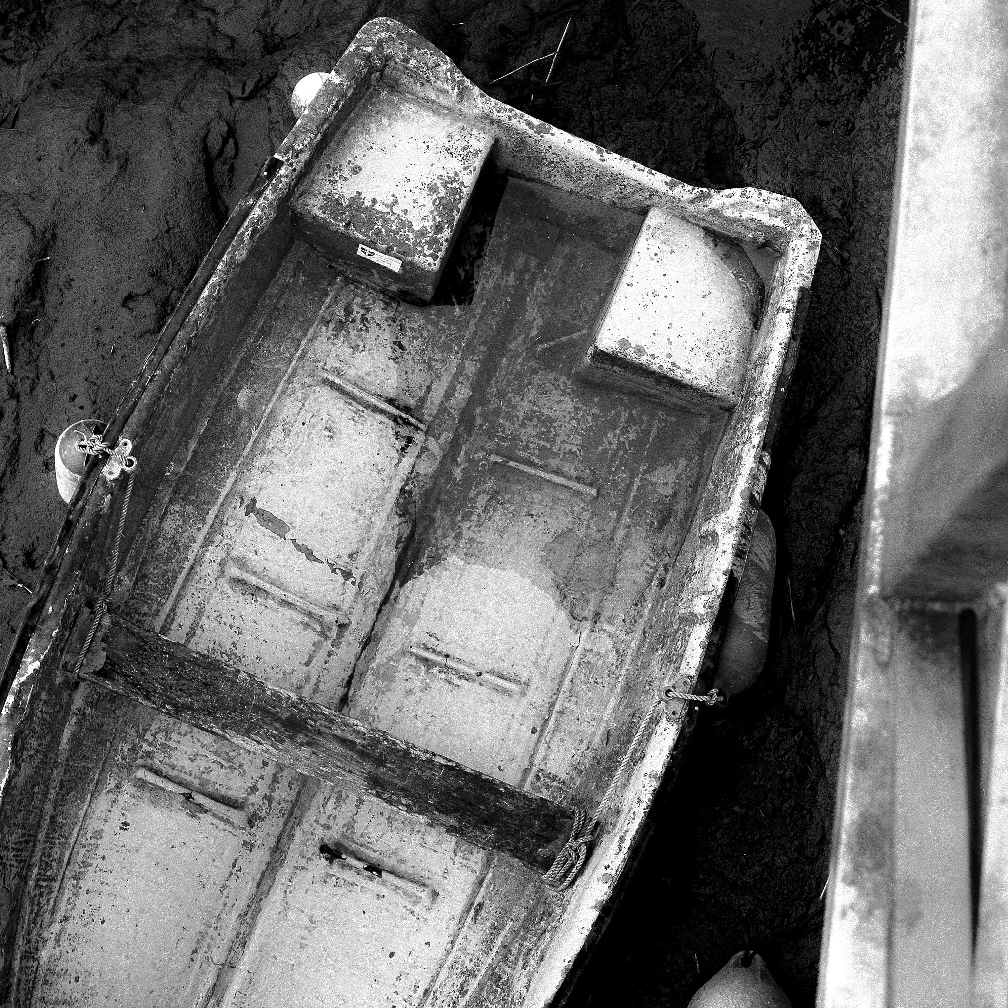 A black and white photo showing a close-up of an old, rusted, and weathered industrial machine or equipment part, possibly a metal container or component, with visible corrosion, dirt, and grime.