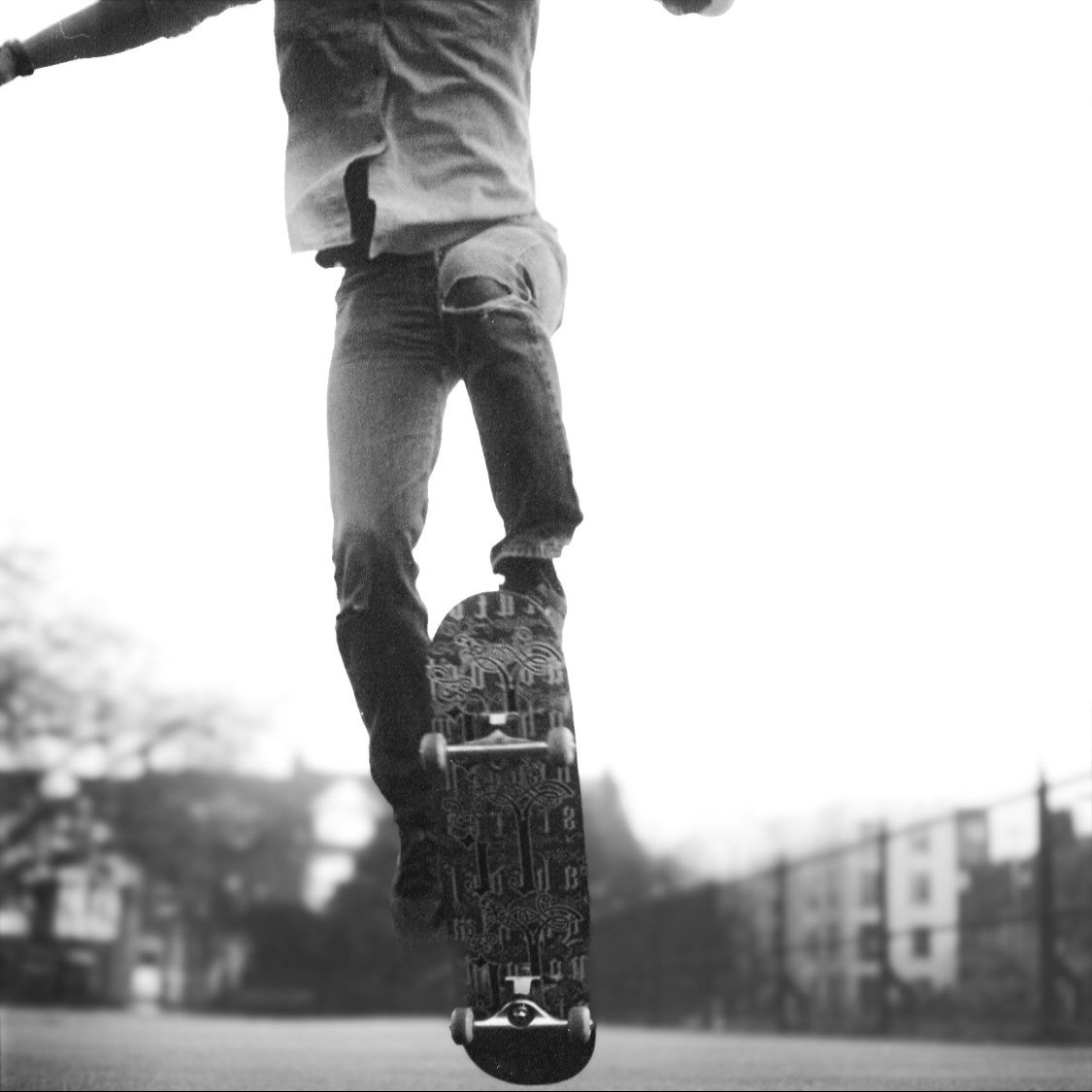 A person performing a skateboarding trick on an outdoor court, captured from a low angle, in black and white.