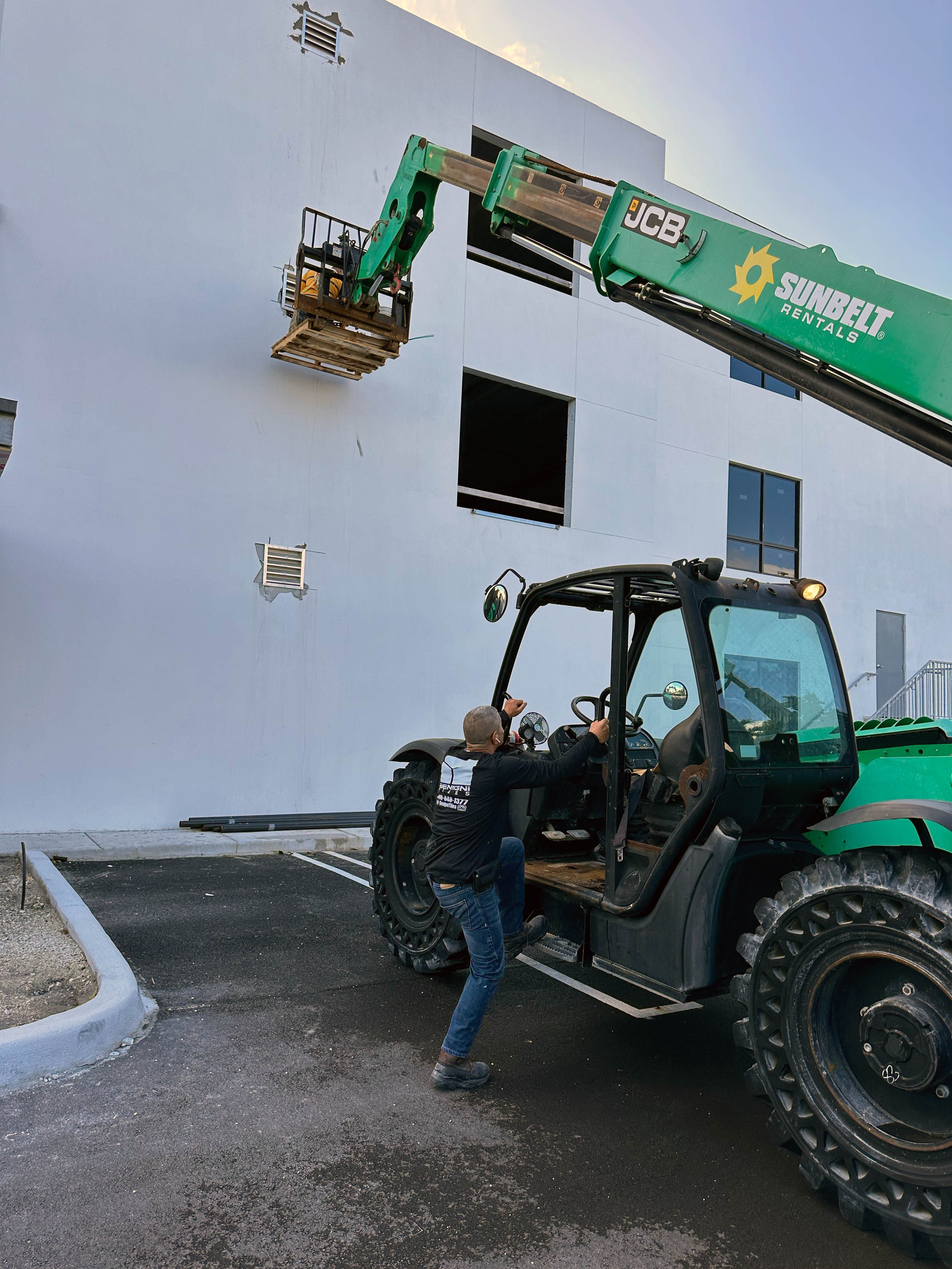 A crane at a construction site, with a worker and a person on the phone in a parking lot