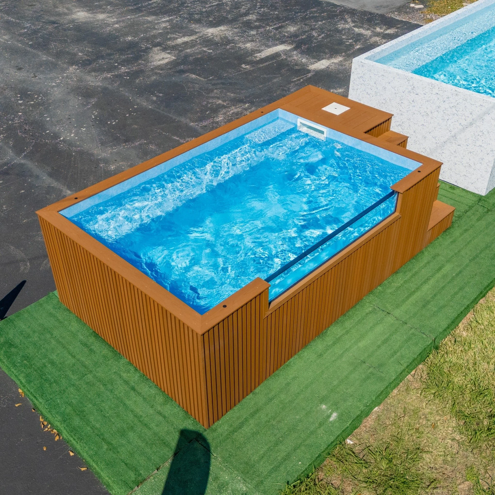 A above-ground pool with blue water in a wooden structure, located in an outdoor area with a dark concrete floor and a green lawn.