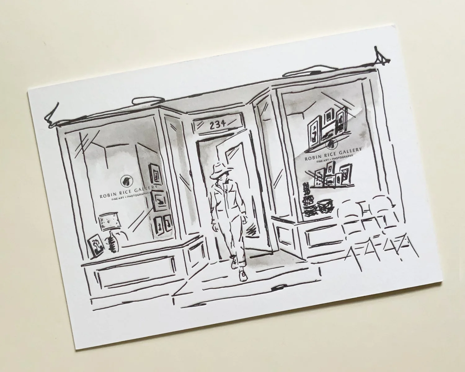 Black and white sketch of the storefront of Robin Rice Gallery, with a person walking out the door. The gallery's window displays art and photography, with chairs outside.