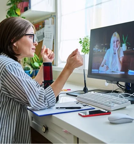 Woman having a video call with a smiling woman on a computer screen in a home office.