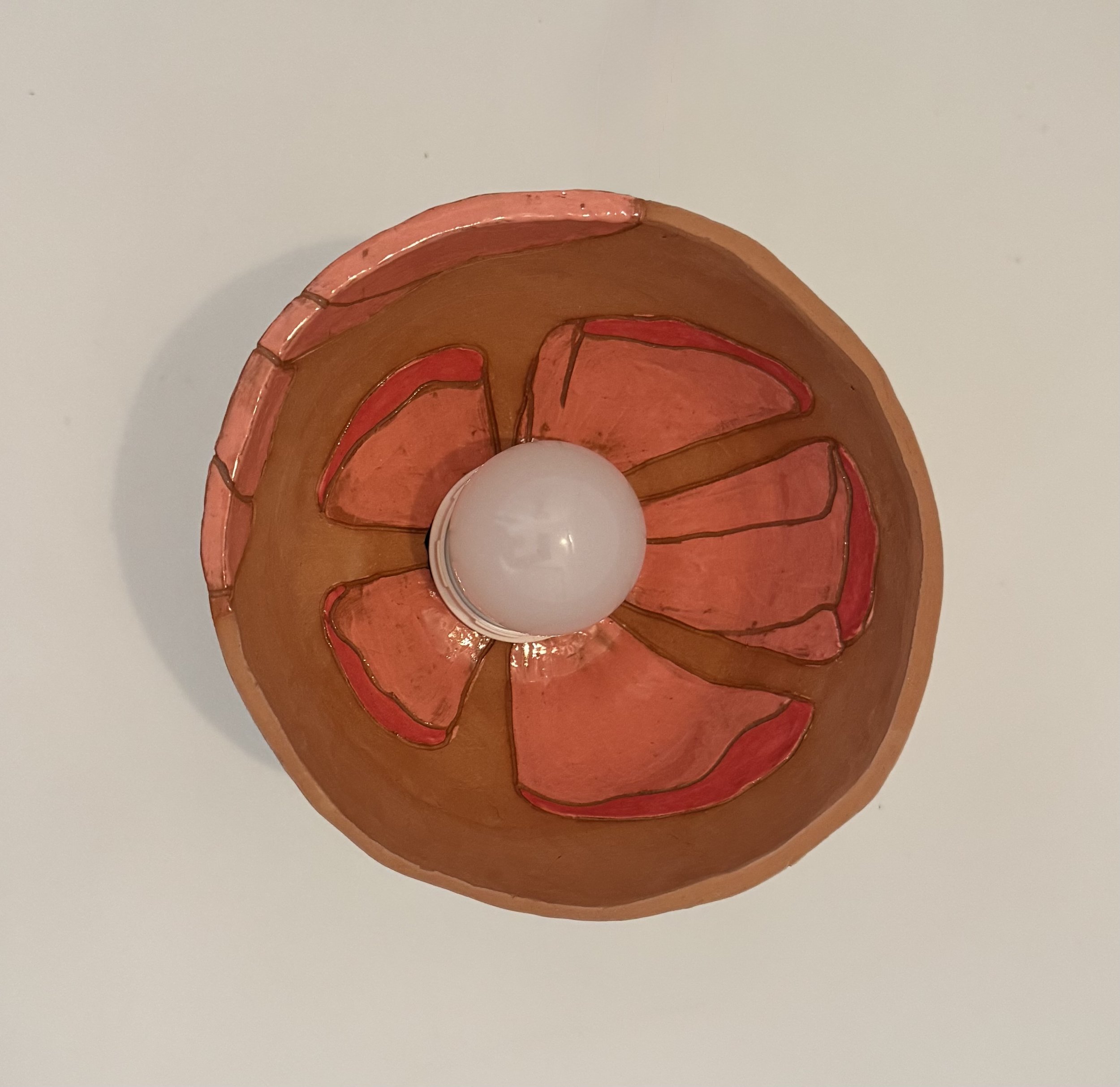 Close-up view of a decorative ceramic piece with curved, layered red and pink sections, placed on a white surface.