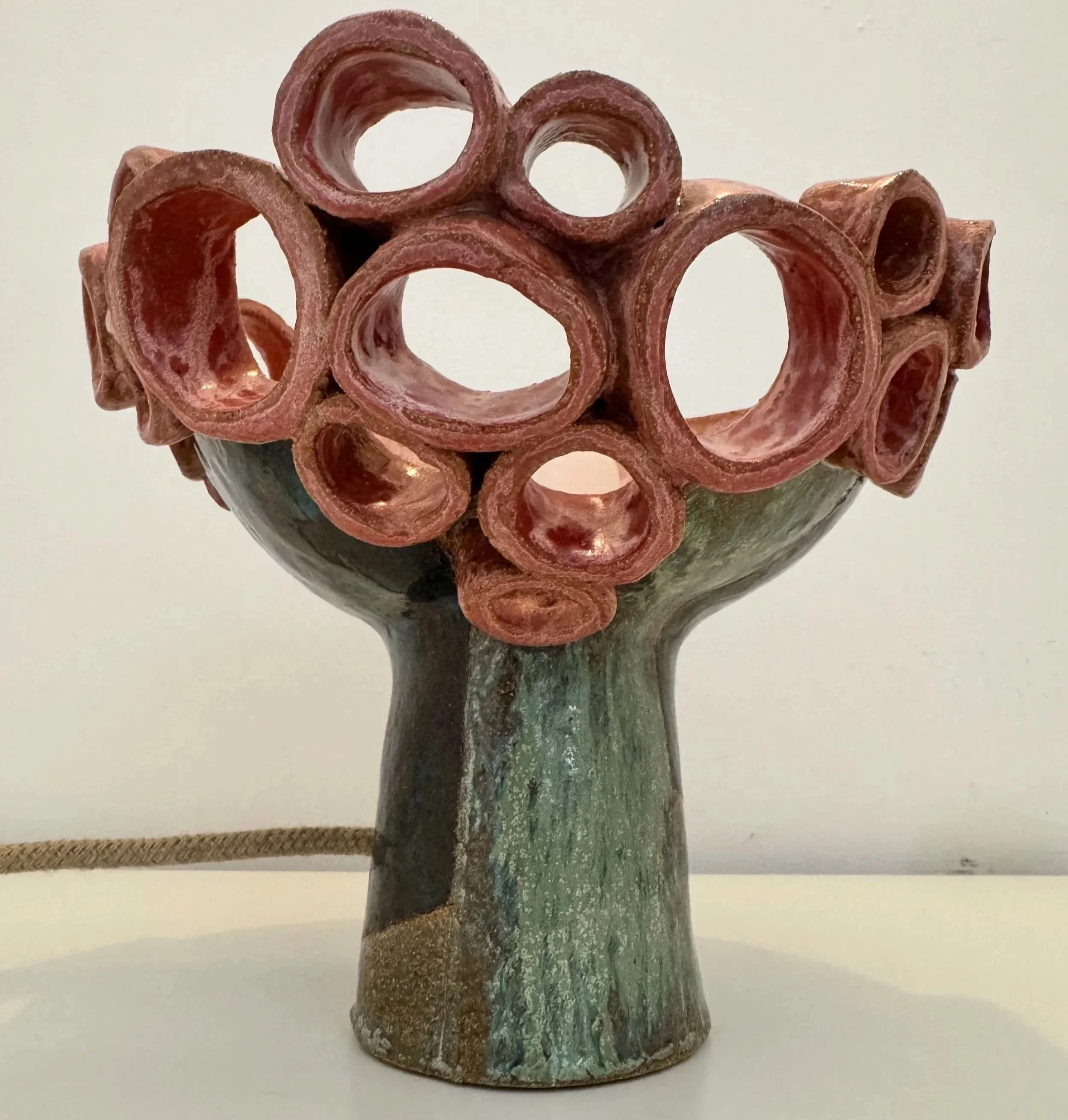A decorative sculpture of a tree with a rounded, hollow, flower-like top in rust and green colors.