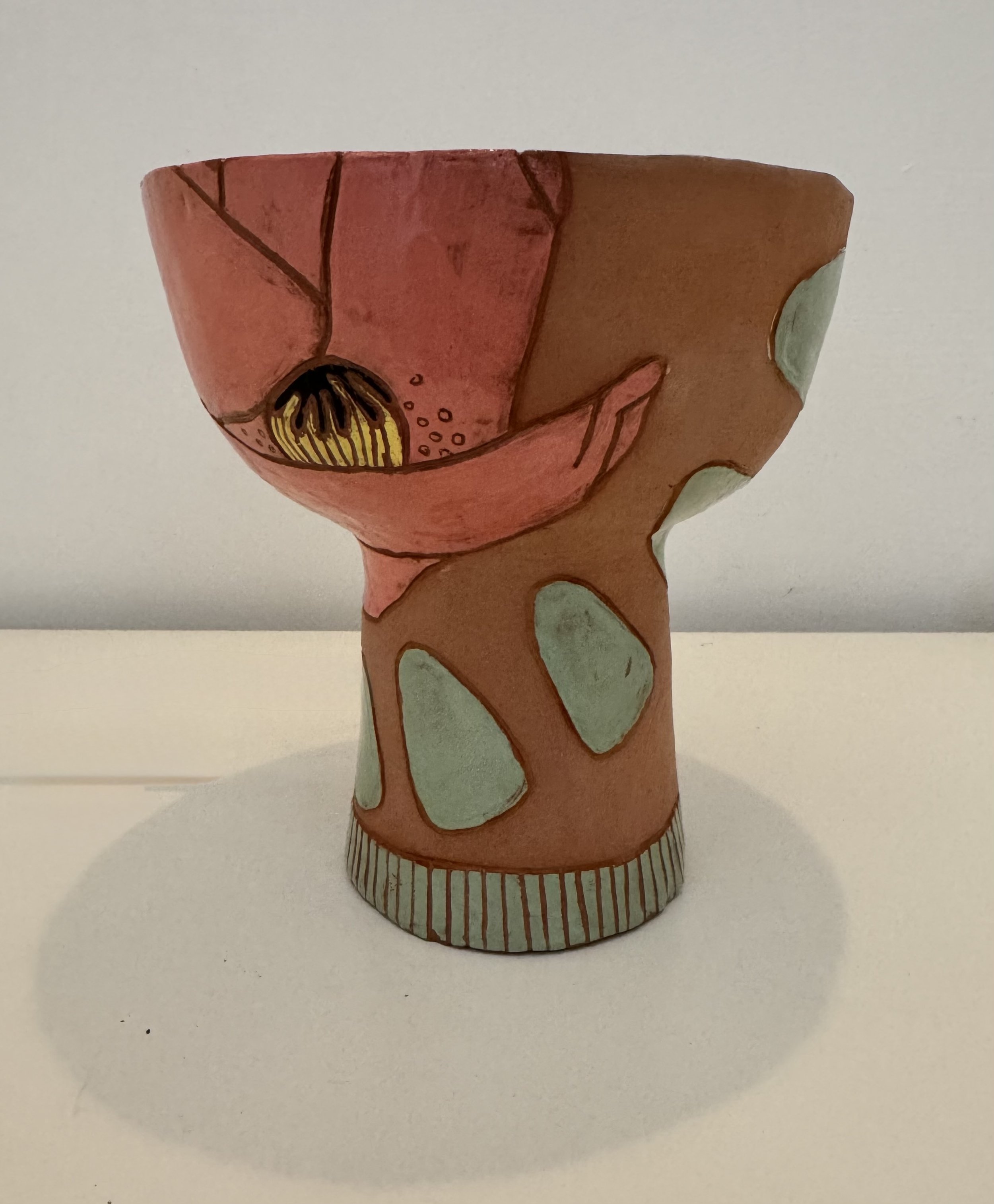 A hand-painted ceramic or paper mache decorative piece resembling a gnome with a large red hat, green patches, and a yellow and black detail on its face, held in a hand.