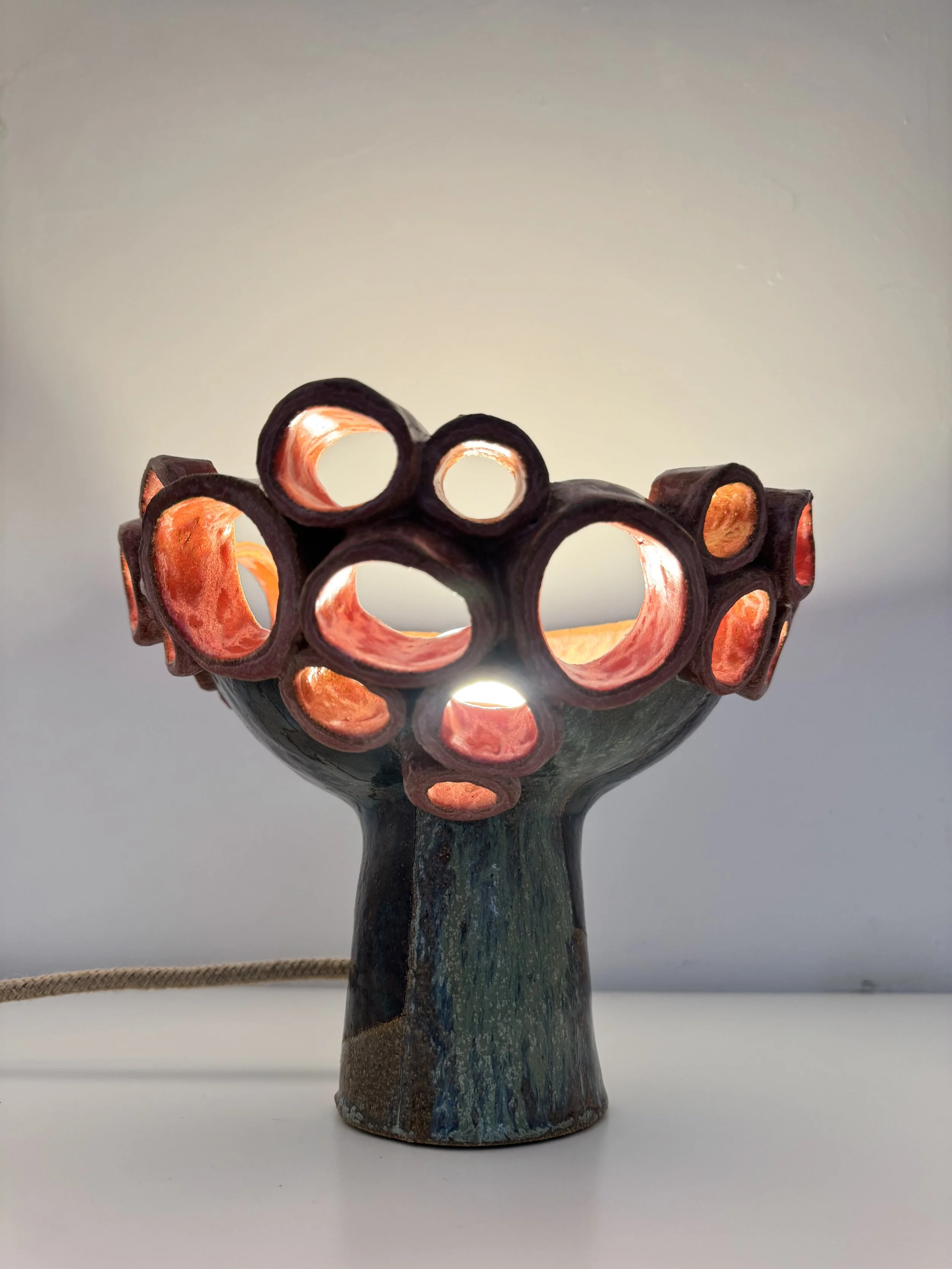 A ceramic vase with a textured, multicolored glaze and an openwork top featuring multiple circular openings, set against a plain white background.