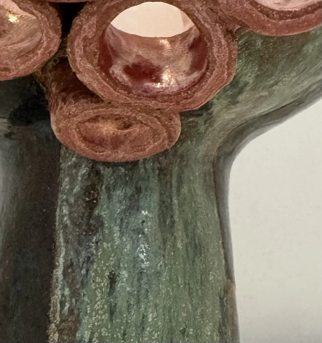 Close-up of a part of a sculpture with several pink-brown hollow tube structure on top of a greenish textured base. part of a hand made ceramic lamp