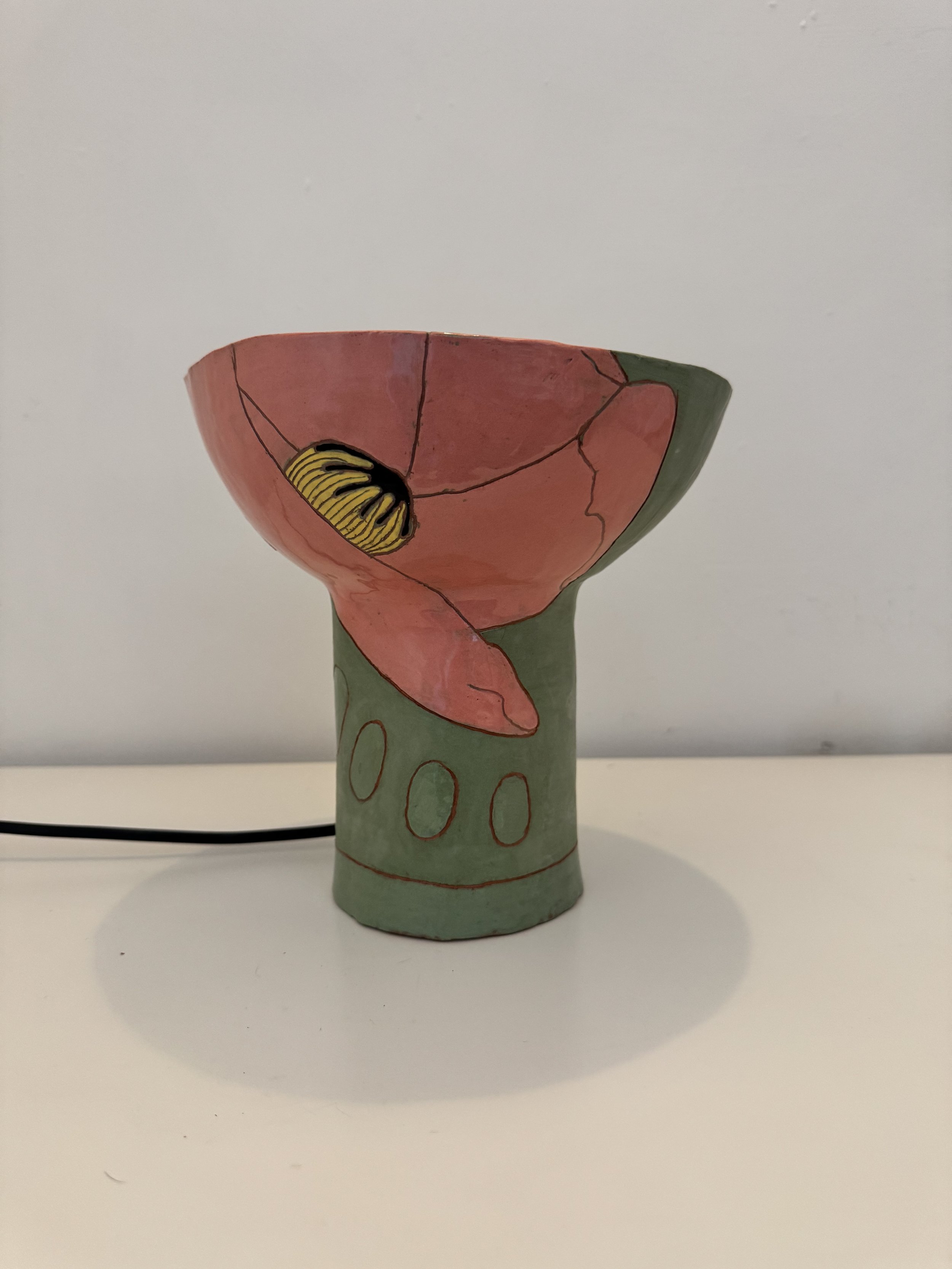 Handmade ceramic cup decorated with painted flower design and abstract patterns in pink, green, and yellow on a white background.