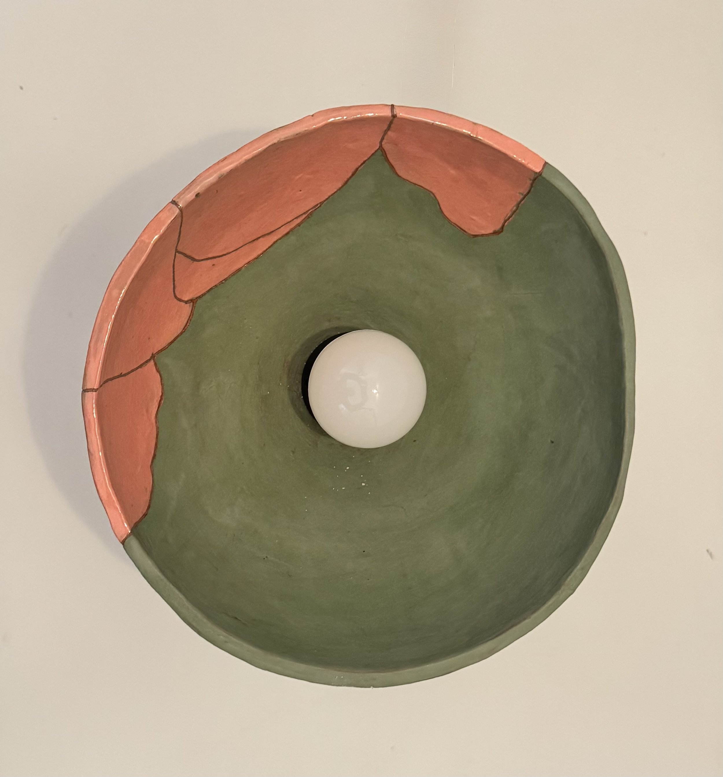 Close-up of a handmade ceramic bowl with a green interior and pink rim, decorated with leaf or petal shapes outlined in black.