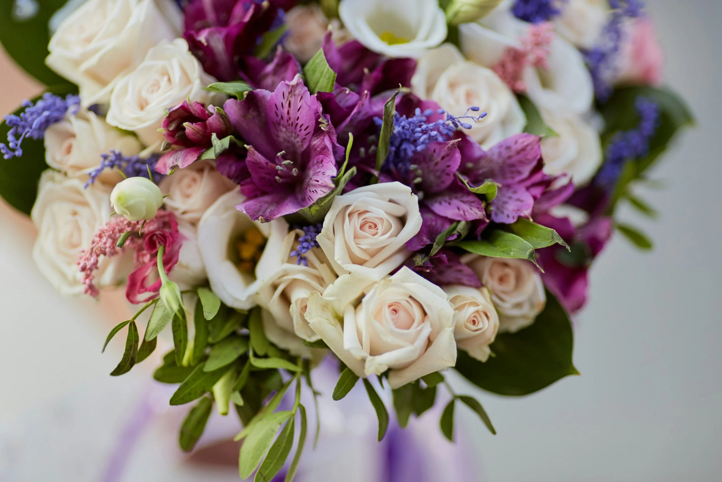 Close-up of a bouquet of white roses, purple flowers, and greenery.