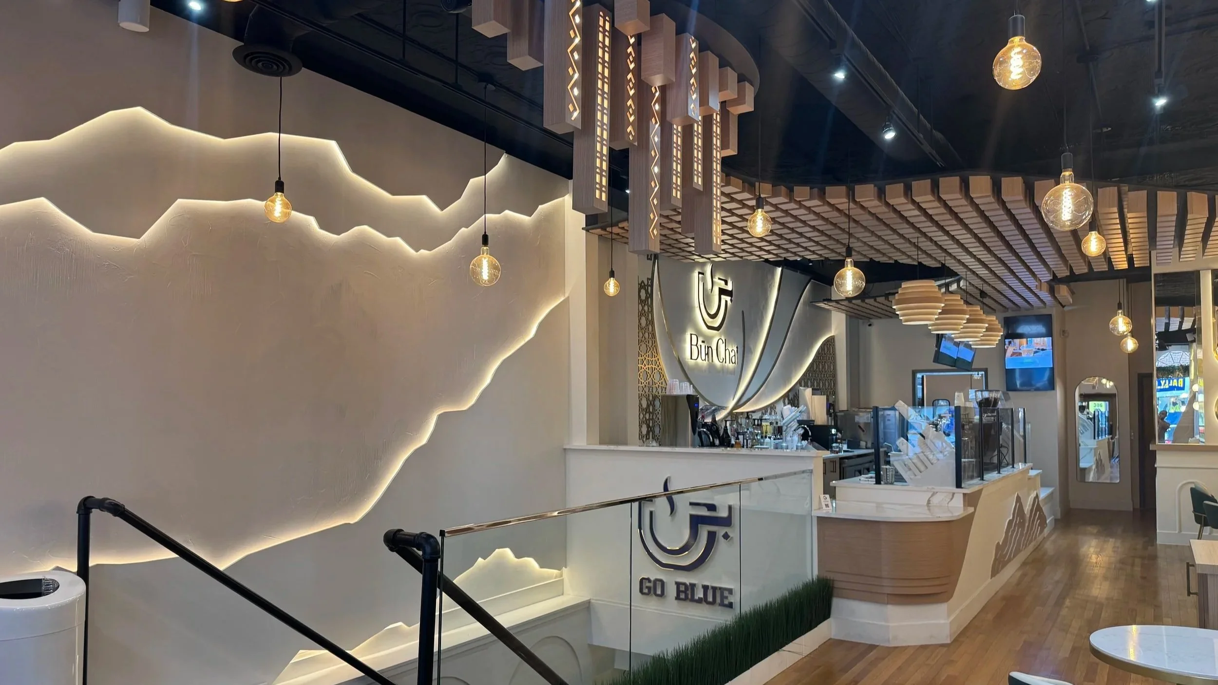 Interior of Bun Chai Yemeni Coffee & Tea in Ann Arbor, Michigan, featuring an illuminated mountain wall, pendant lighting, and coffee bar.
