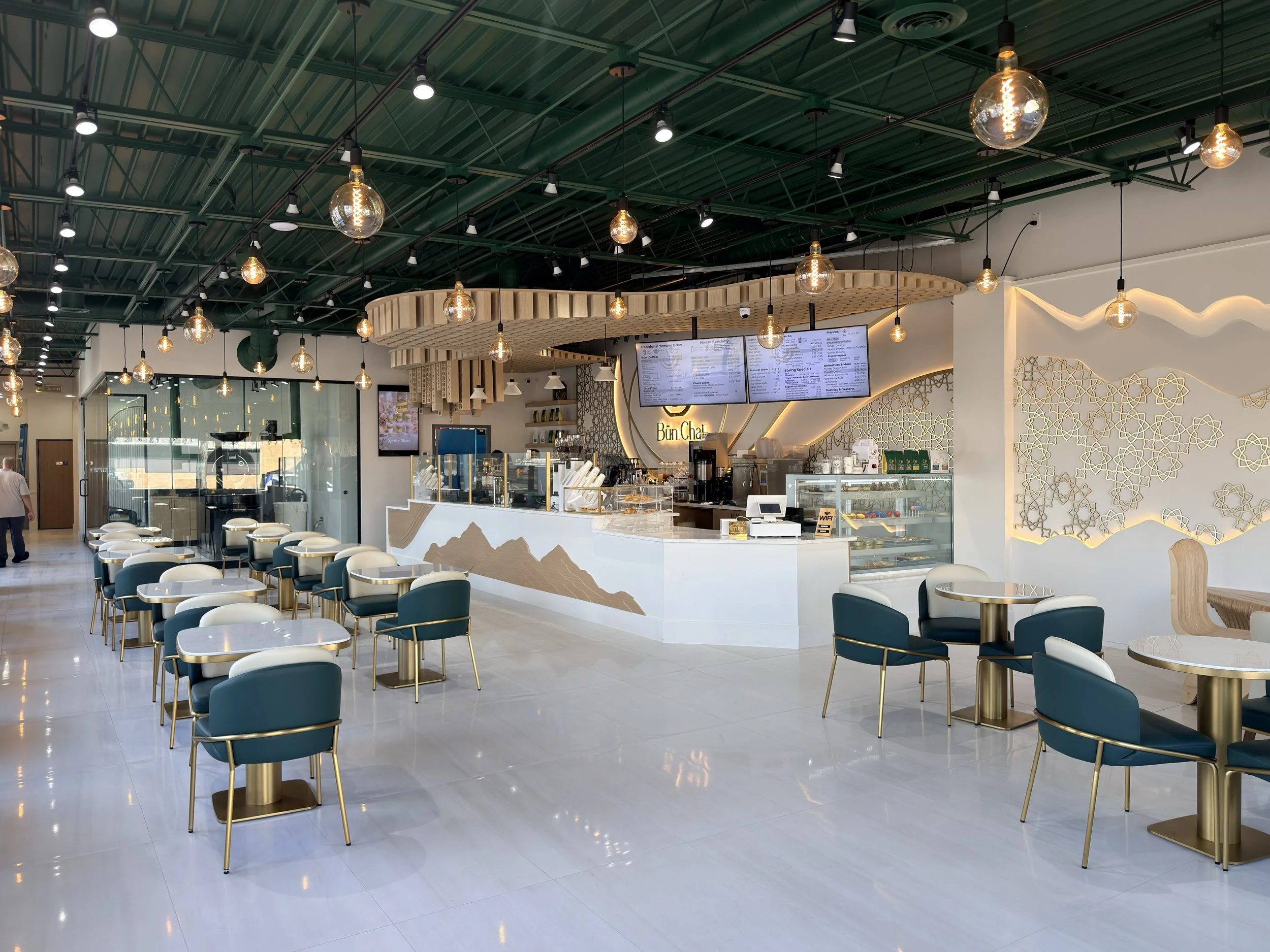 Interior of Bun Chai Yemeni Coffee & Tea in Hamtramck, Michigan, featuring café seating, illuminated décor, and an in-house coffee roaster.