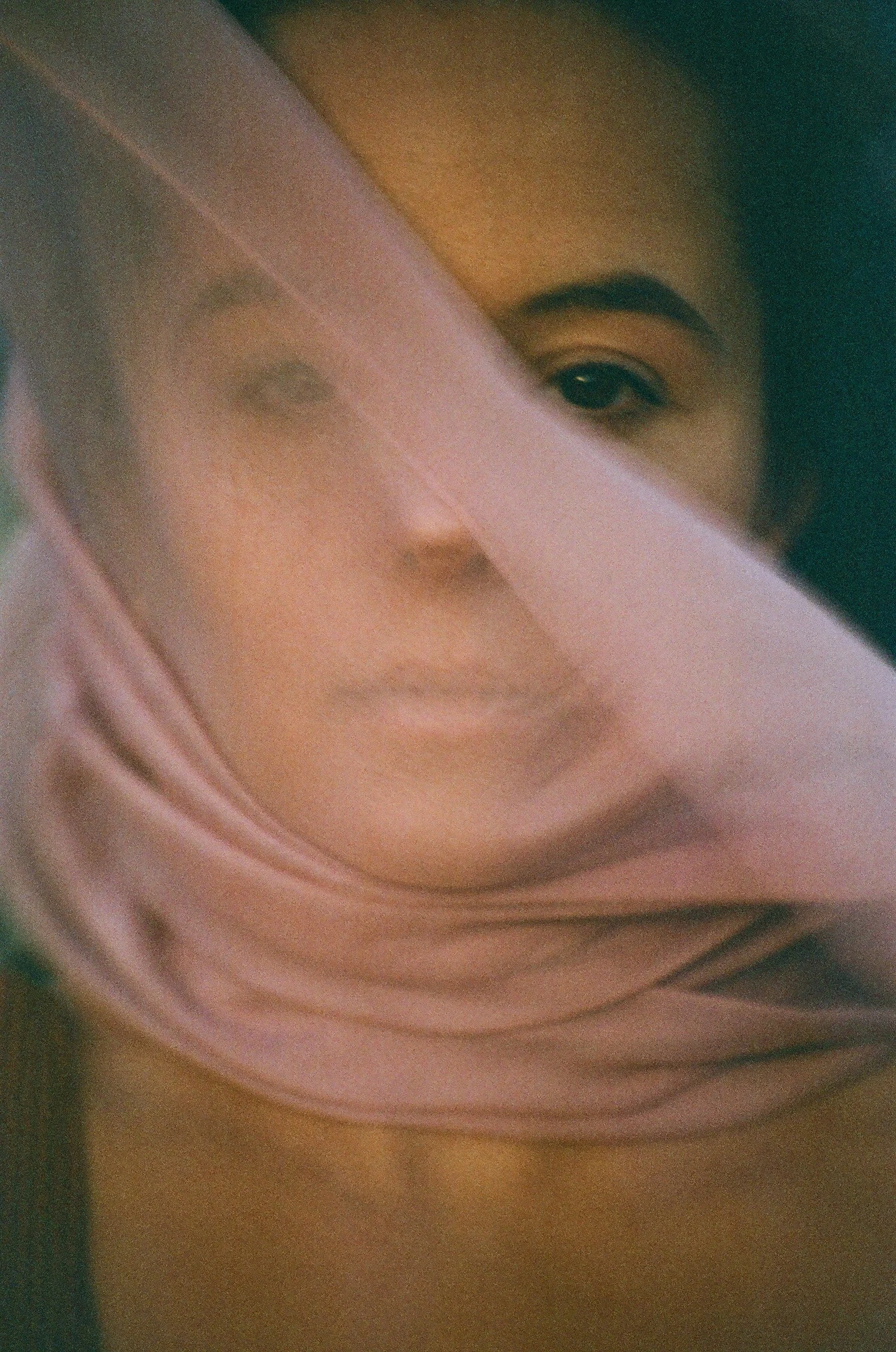 Un portrait flou d'une femme portant une écharpe rose, avec une mise en cachette partielle du visage par des tissus.