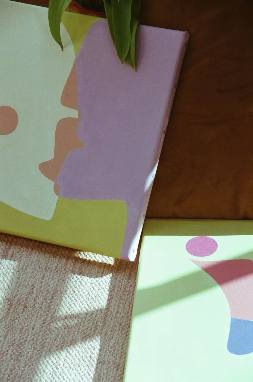 Deux livres avec des couvertures colorées et abstraites, posés sur un fauteuil en tissu avec des rayures de lumière naturelle.
