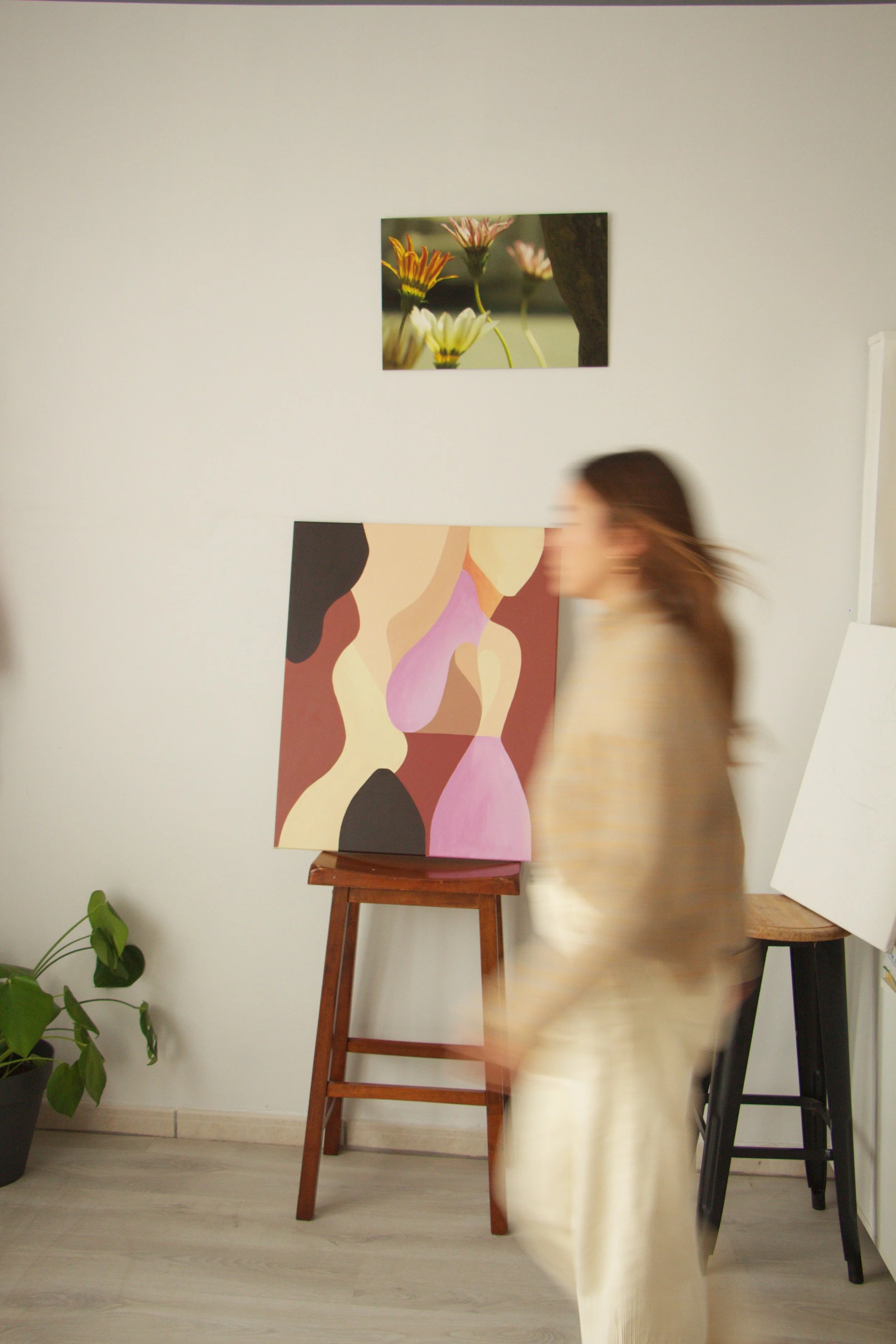 Une femme se déplaçant rapidement devant un mur blanc la rendant flou avec des œuvres d'art suspendues, dont une peinture abstraite colorée et une photo de fleurs.