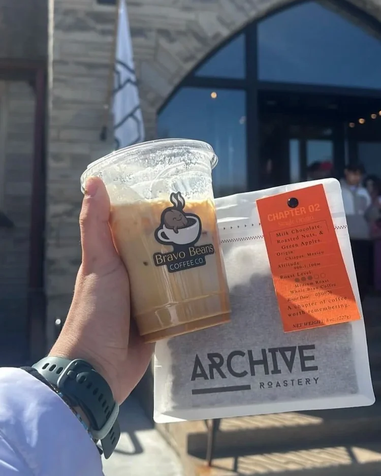 Bravo Beans iced latte held beside a bag of Archive Roastery coffee