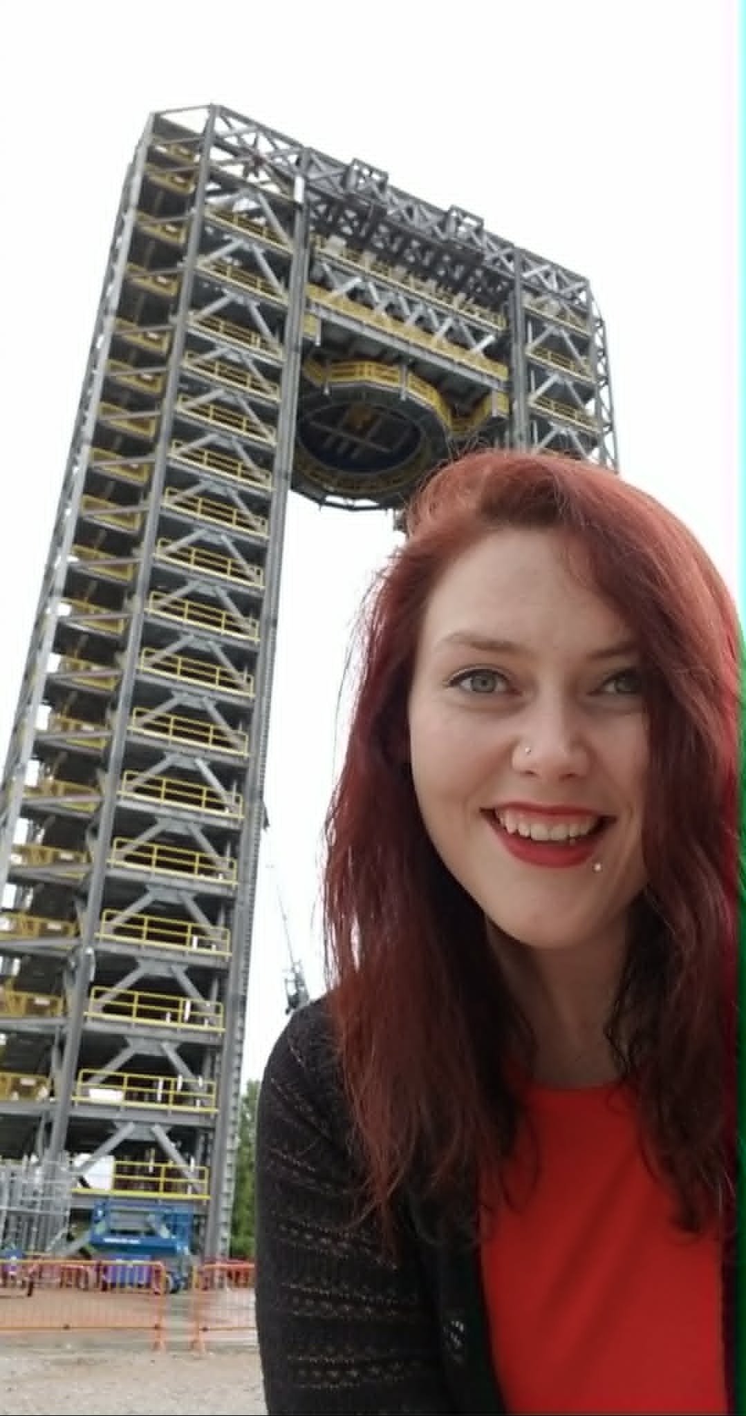 A woman with red hair smiling in front of a large amusement park ride.