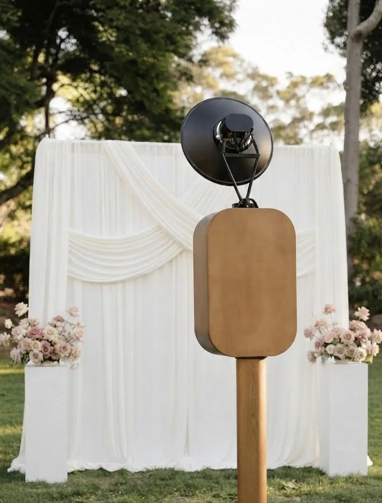 A vintage photobooth with white drapery backdrop and floral accents on both sides