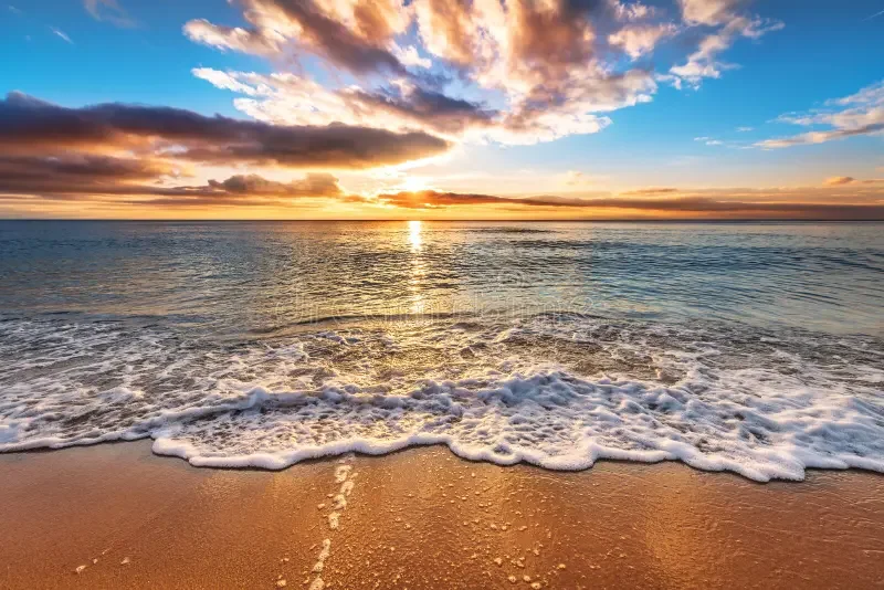 Coucher de soleil sur une plage avec des vagues, ciel orageux coloré d'orange, de rose et de bleu.