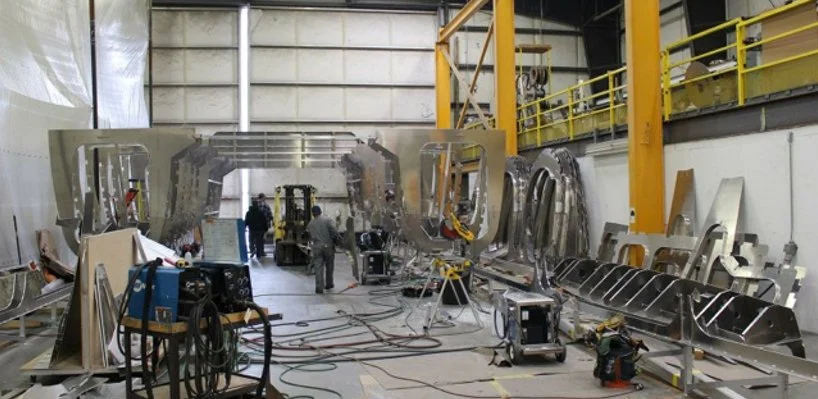 Industrial workshop with metal frames, tools, and workers assembling or repairing large metal structures.
