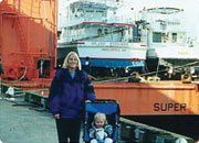 A woman pushing a stroller with a child in front of a large orange ship at a harbor.
