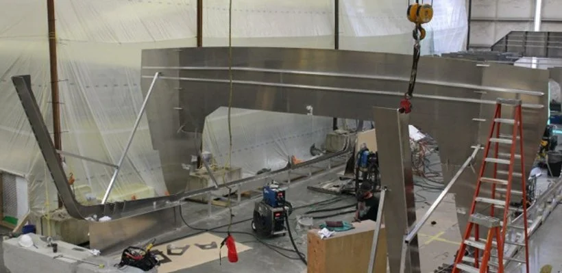 Construction of a large metallic structure in a warehouse with tools and ladders around.
